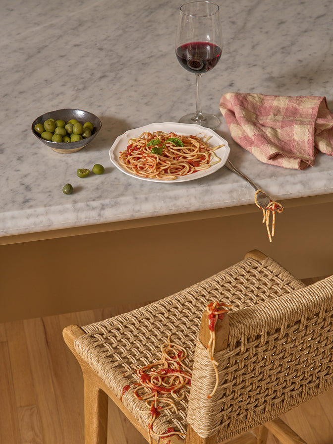 Plate of spaghetti with a glass of red wine on a marble countertop.