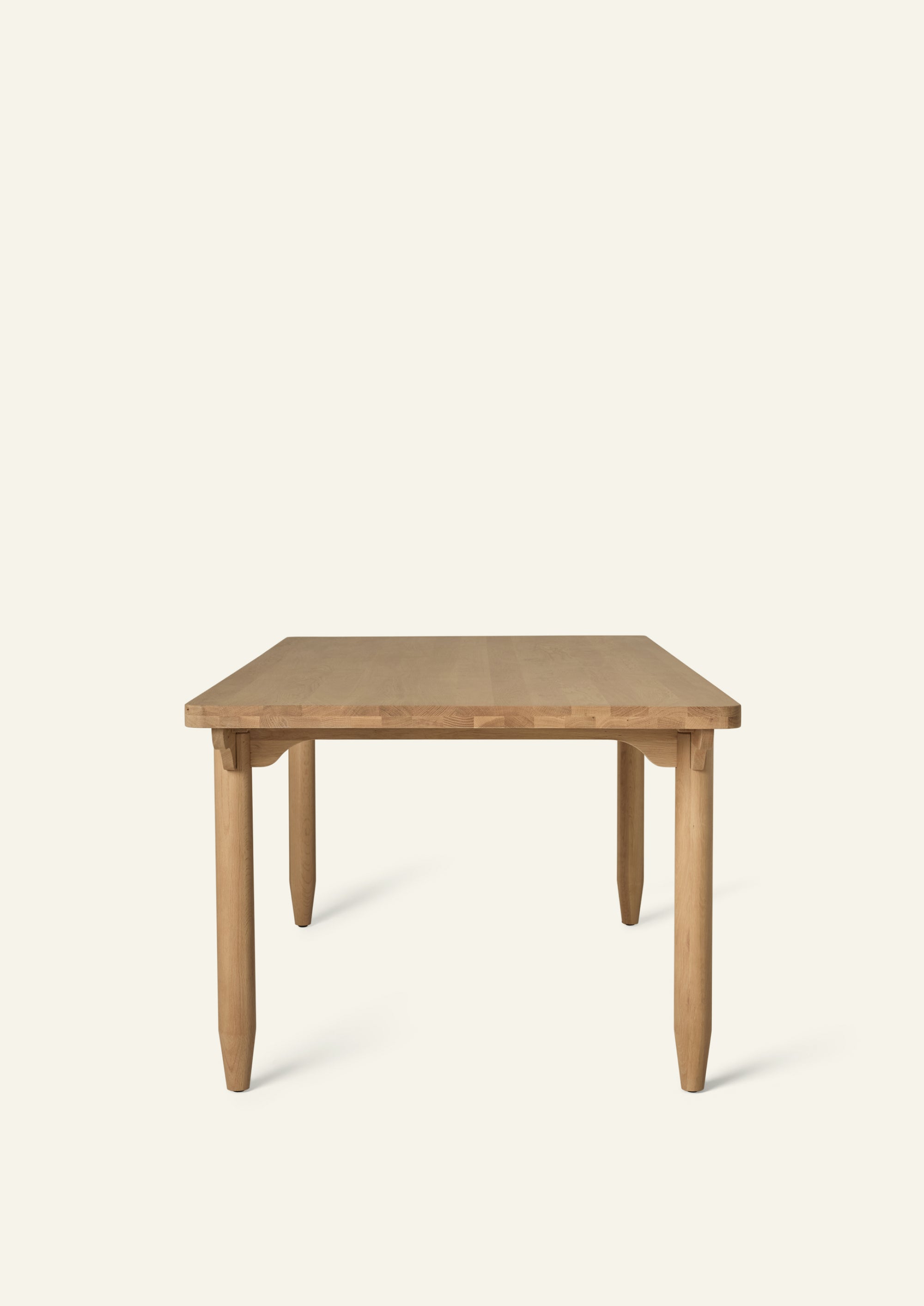 Front view of the rectangular dining table highlighting its solid oak construction, rounded pencil legs, and decorative scalloped apron. Generous proportions provide ample seating while maintaining an airy, elegant profile.