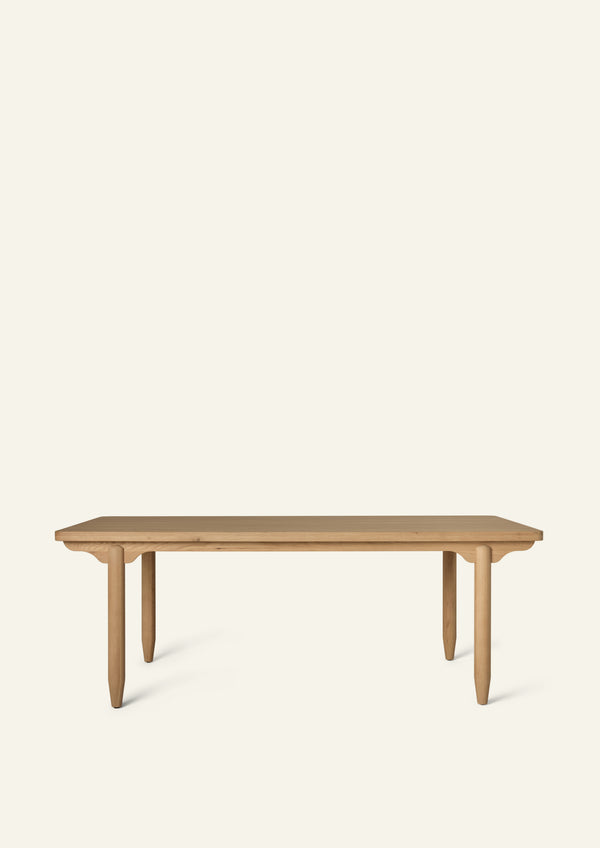 Side profile of the dining table showing its substantial tabletop, scalloped apron, and tapered pencil legs. The clean lines and sculptural details create a timeless silhouette suited to a range of interior styles.