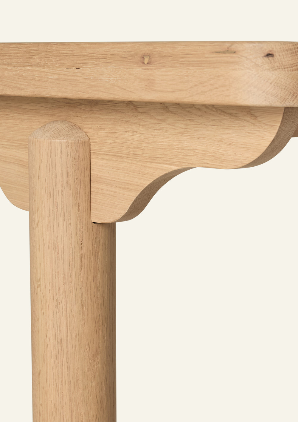 Close-up of the table’s rounded leg and scalloped apron detail, showcasing the natural oak grain and thoughtful craftsmanship. The sculptural silhouette balances traditional inspiration with clean, modern lines.