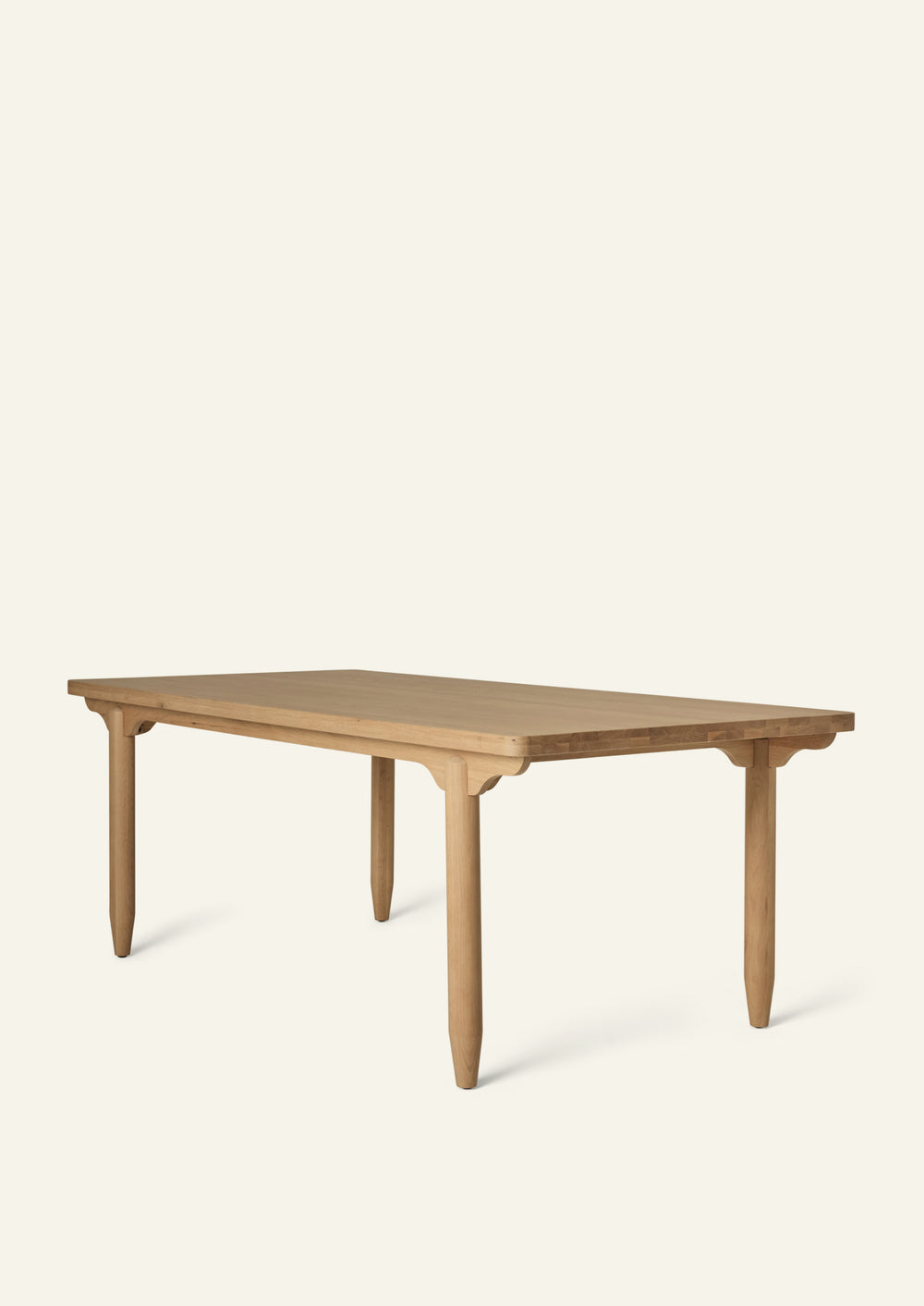 Three-quarter view of the dining table in White Oak. Crafted from solid oak, the table features softly rounded corners, sculptural pencil legs, and scalloped apron detailing that lends a collected, timeless character.