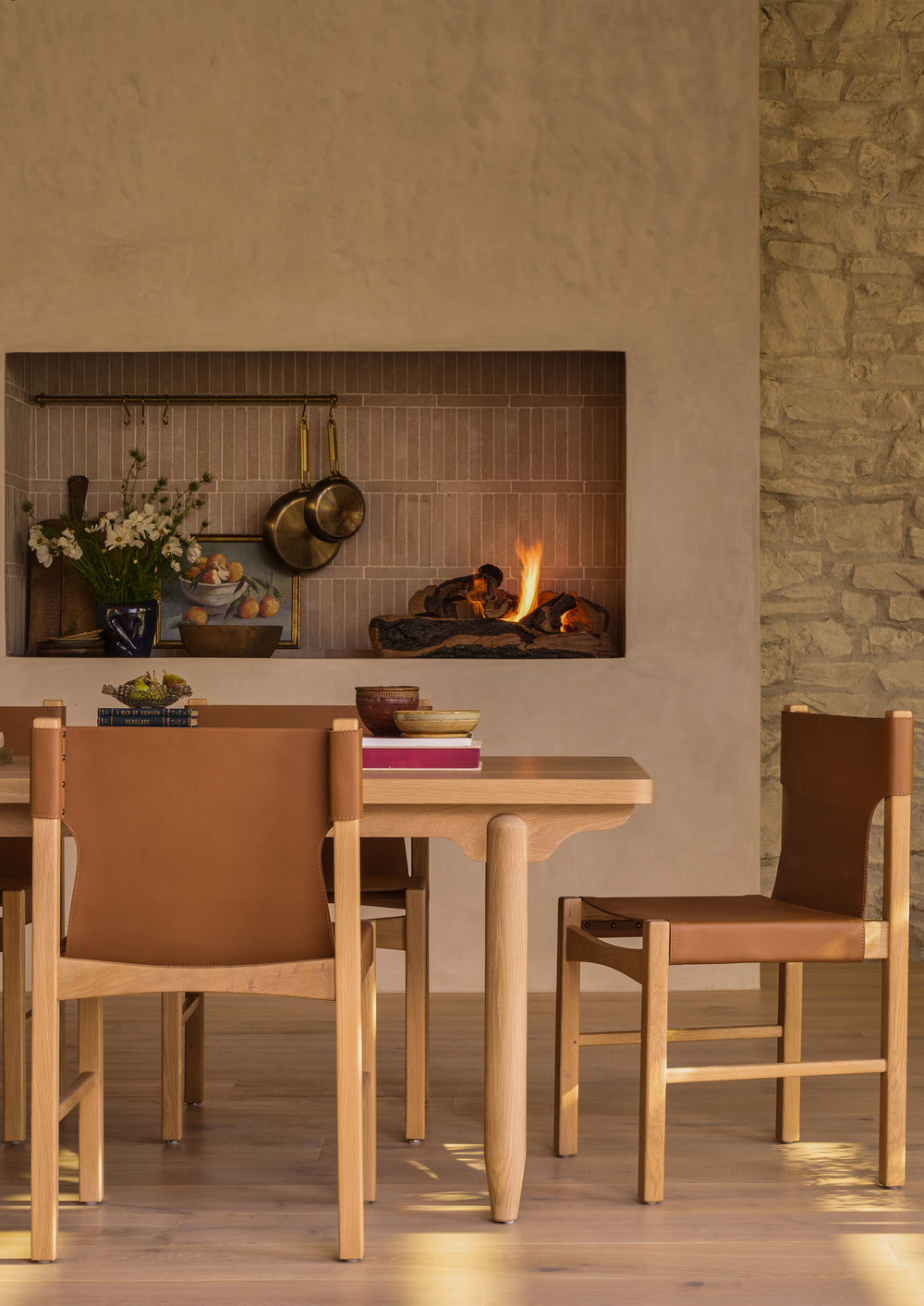 The dining table styled in a contemporary dining room with Henrik leather dining chairs and a fireplace backdrop. The warm oak finish and refined detailing bring softness and character to everyday meals and special occasions alike.
