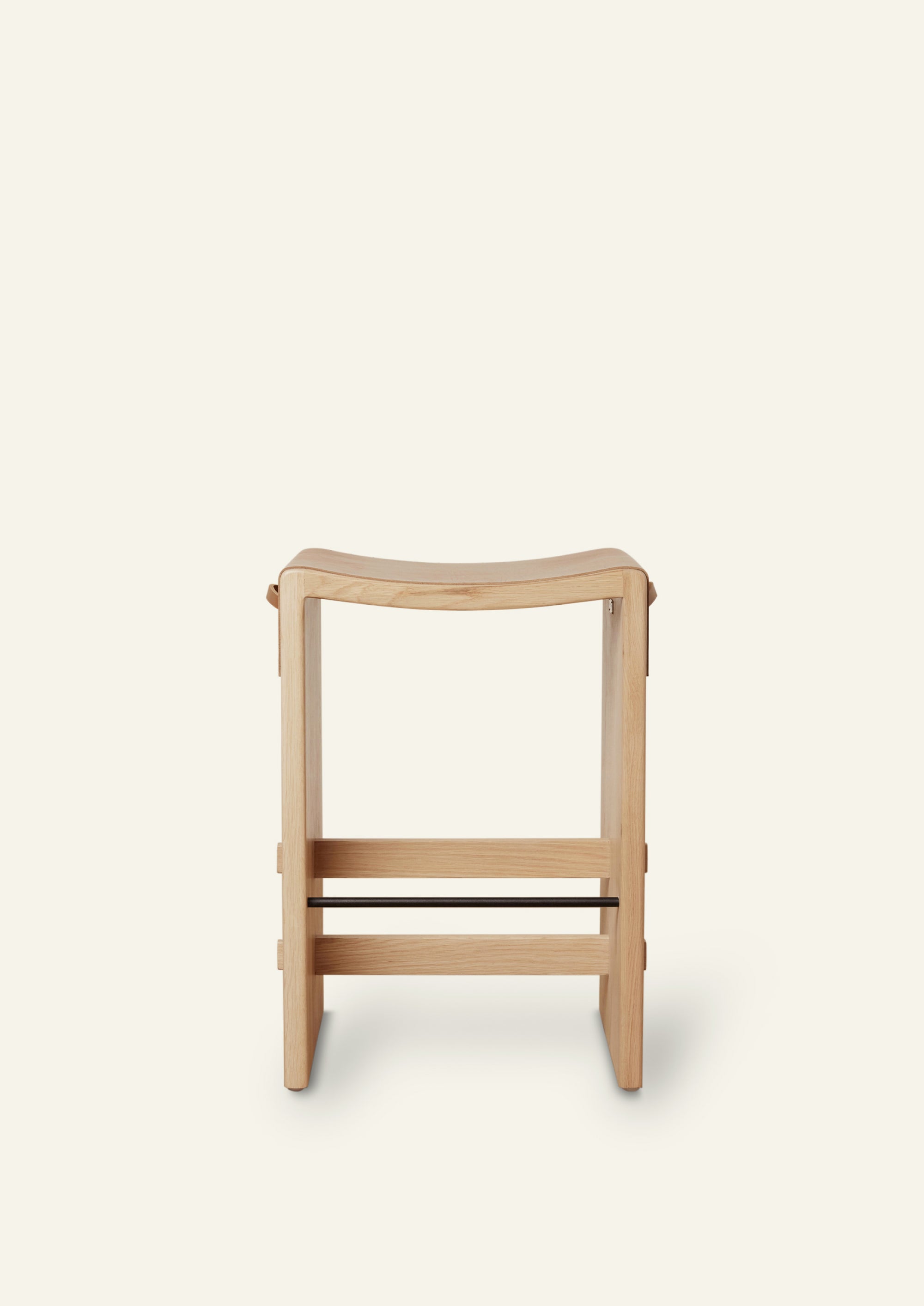 A front view of a white oak counter stool with waterfall cognac leather wrapped on the seat. Powder coated steel footrest sits towards the bottom of the stool. 