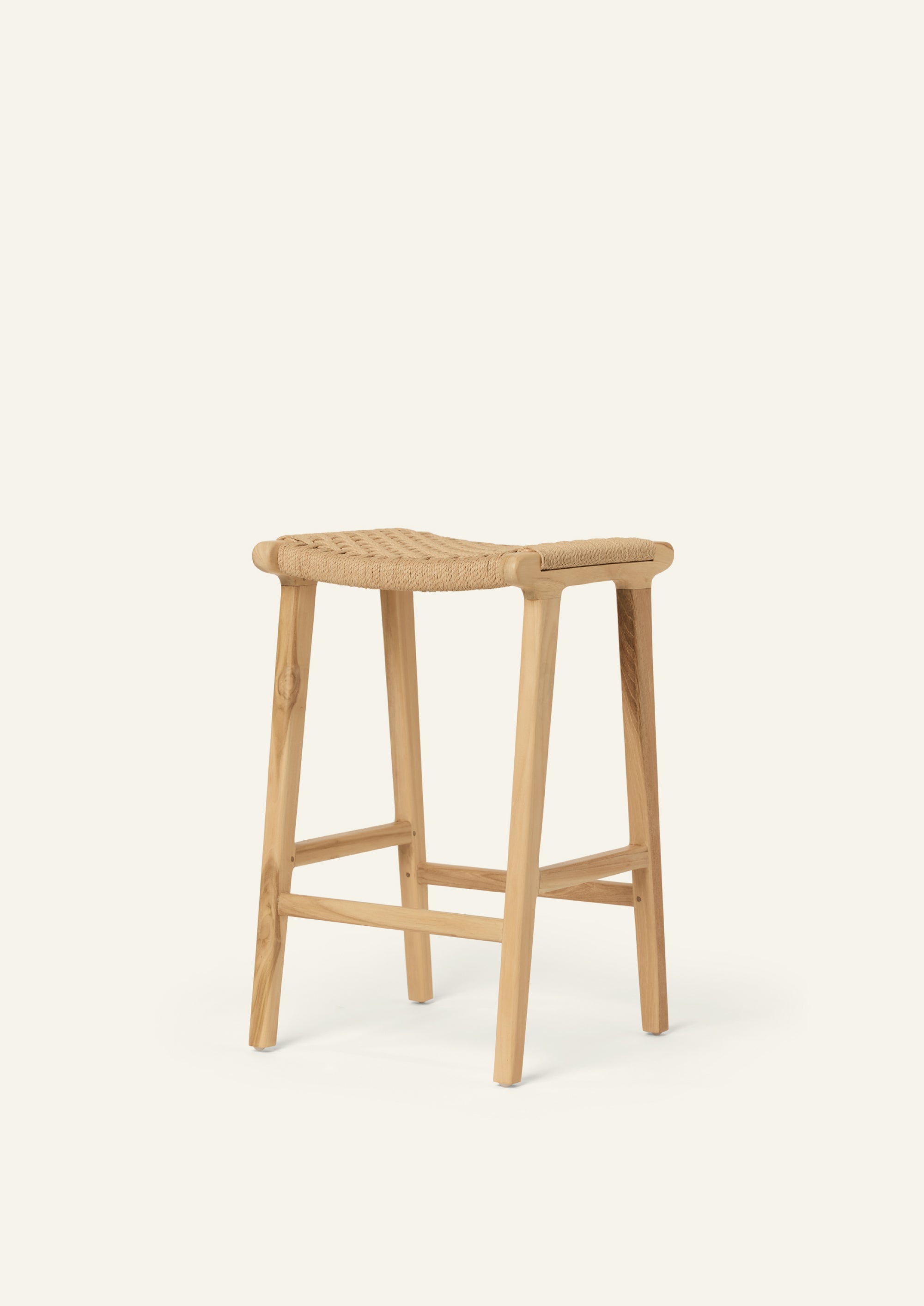 Angled view of the Bali Counter Stool in solid teak with a woven paper cord seat. The stool’s architectural form and natural materials make it well suited for casual, elevated living spaces.