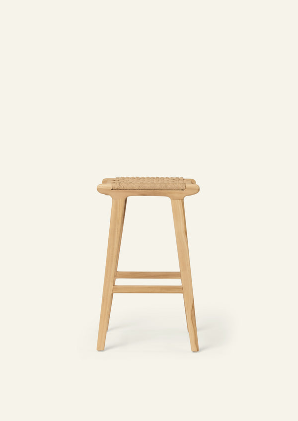 Side profile of the Bali Counter Stool crafted from solid teak with a handwoven natural paper cord seat. The gently tapered legs and clean silhouette create a light, sculptural presence.