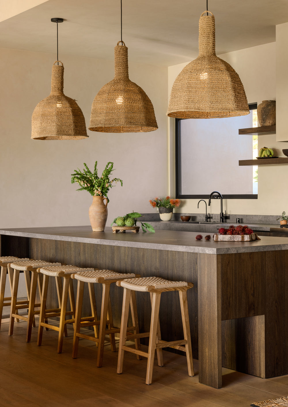 Bali Counter Stools styled around a large kitchen island beneath woven pendant lights. The stools demonstrate the collection’s ability to bring warmth, texture, and casual sophistication to gathering spaces.