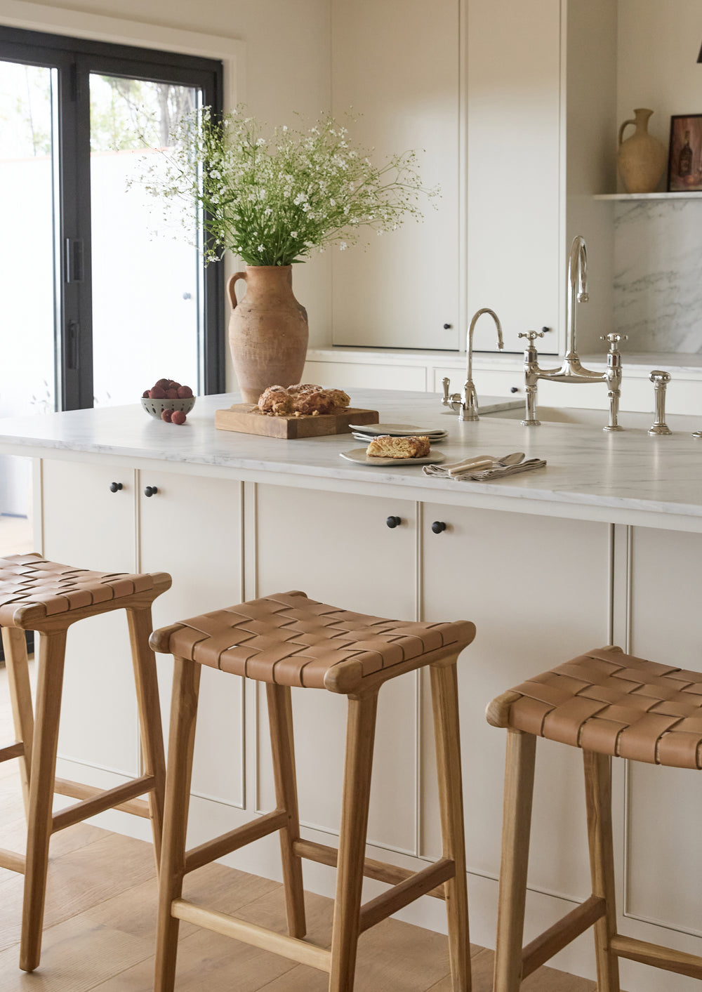 Bali Counter Stools gathered around a bright kitchen island. The warm leather seats and white oak frames add natural texture and casual sophistication to the space.