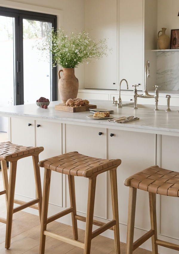 Bali Counter Stools gathered around a bright kitchen island. The warm leather seats and white oak frames add natural texture and casual sophistication to the space.