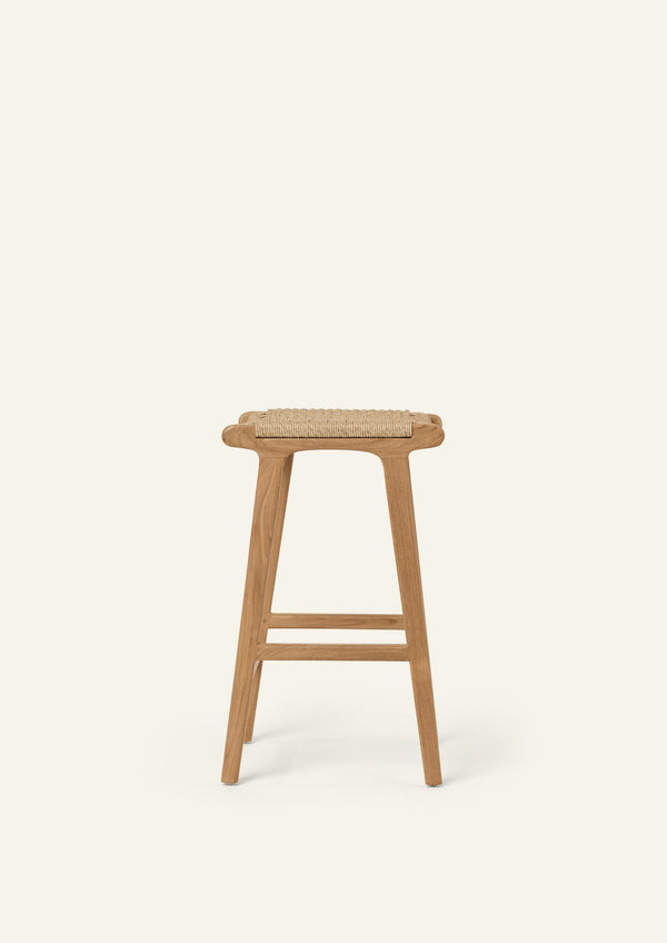 Side profile of the Bali Counter Stool crafted from solid teak and handwoven synthetic paper cord. The sculptural silhouette and gently tapered legs create a light, airy presence suited for both indoor and outdoor spaces.