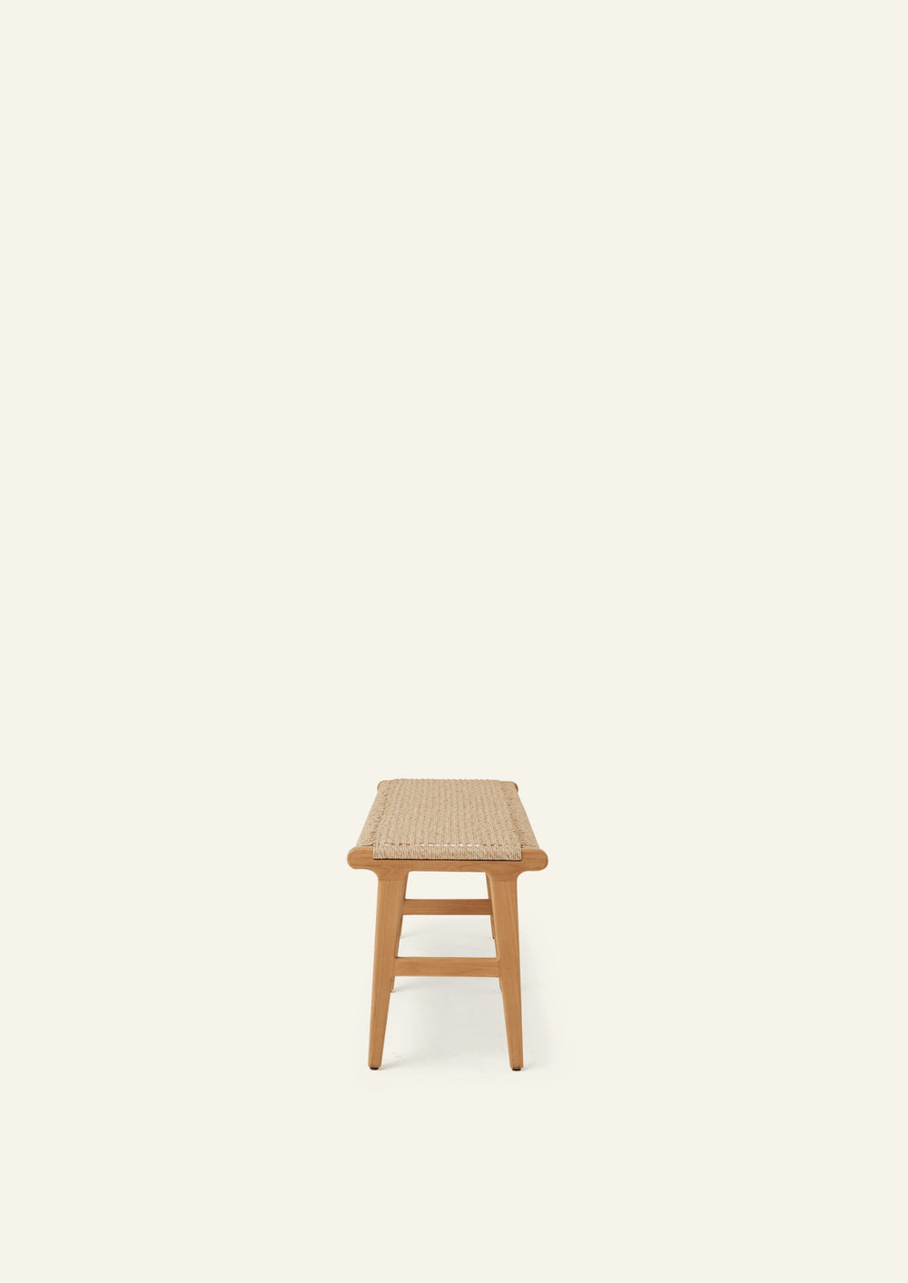 End view of a teak bench featuring a woven synthetic paper cord seat, gently tapered legs, and simple stretcher supports. The streamlined profile emphasizes its lightweight, timeless design.