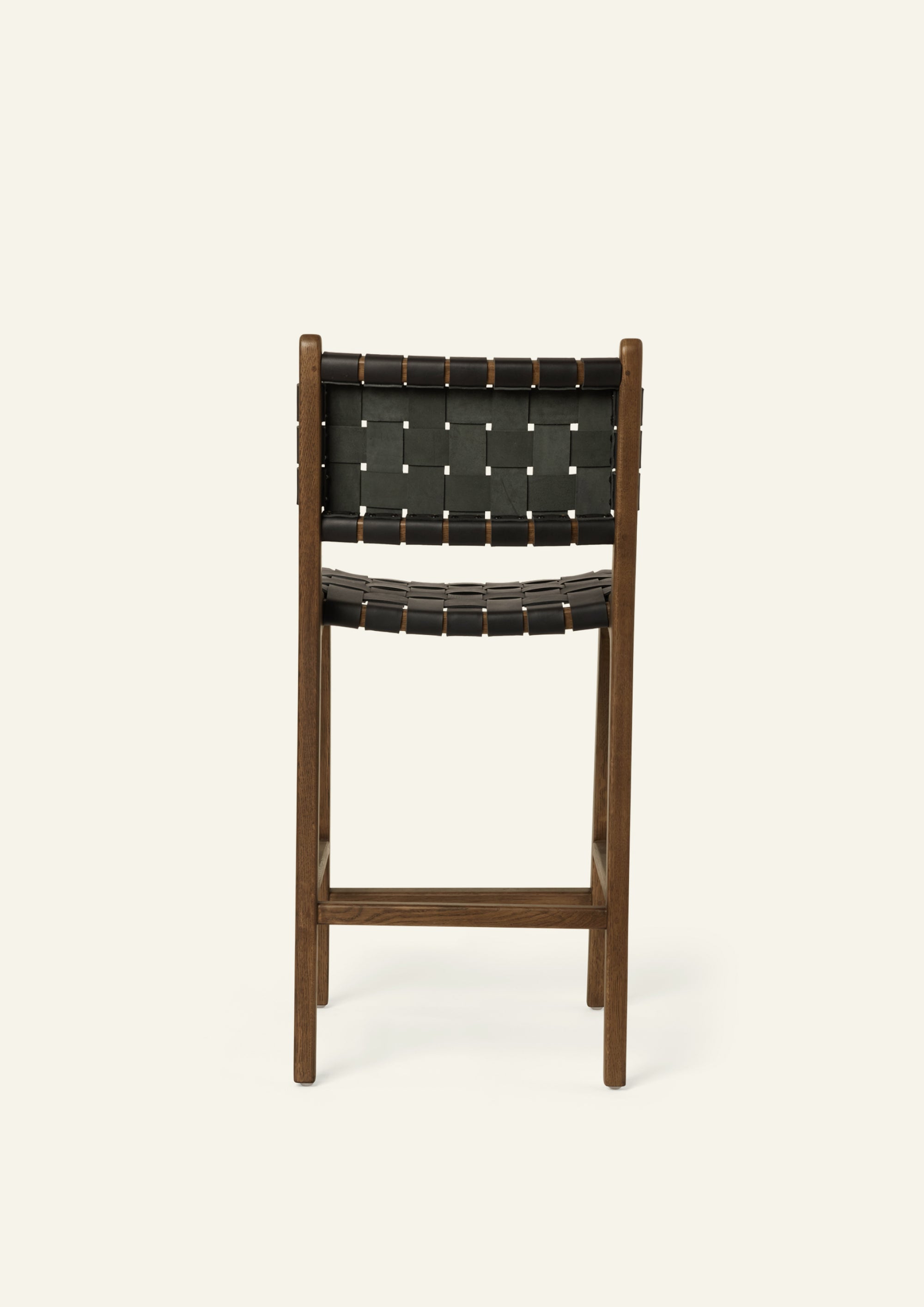 Back view of the Bali Counter Stool in solid brown oak with handwoven black leather, shown in a three-quarter view.