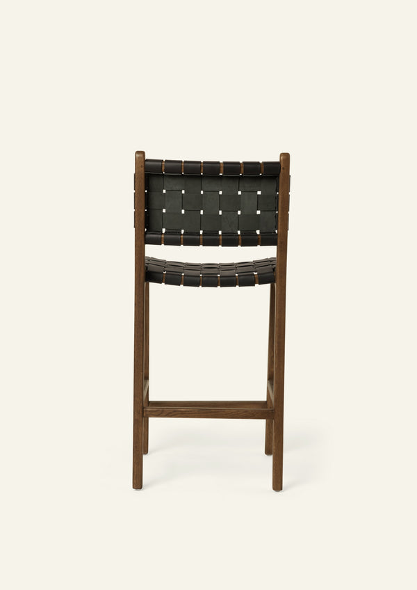 Back view of the Bali Counter Stool in solid brown oak with handwoven black leather, shown in a three-quarter view.