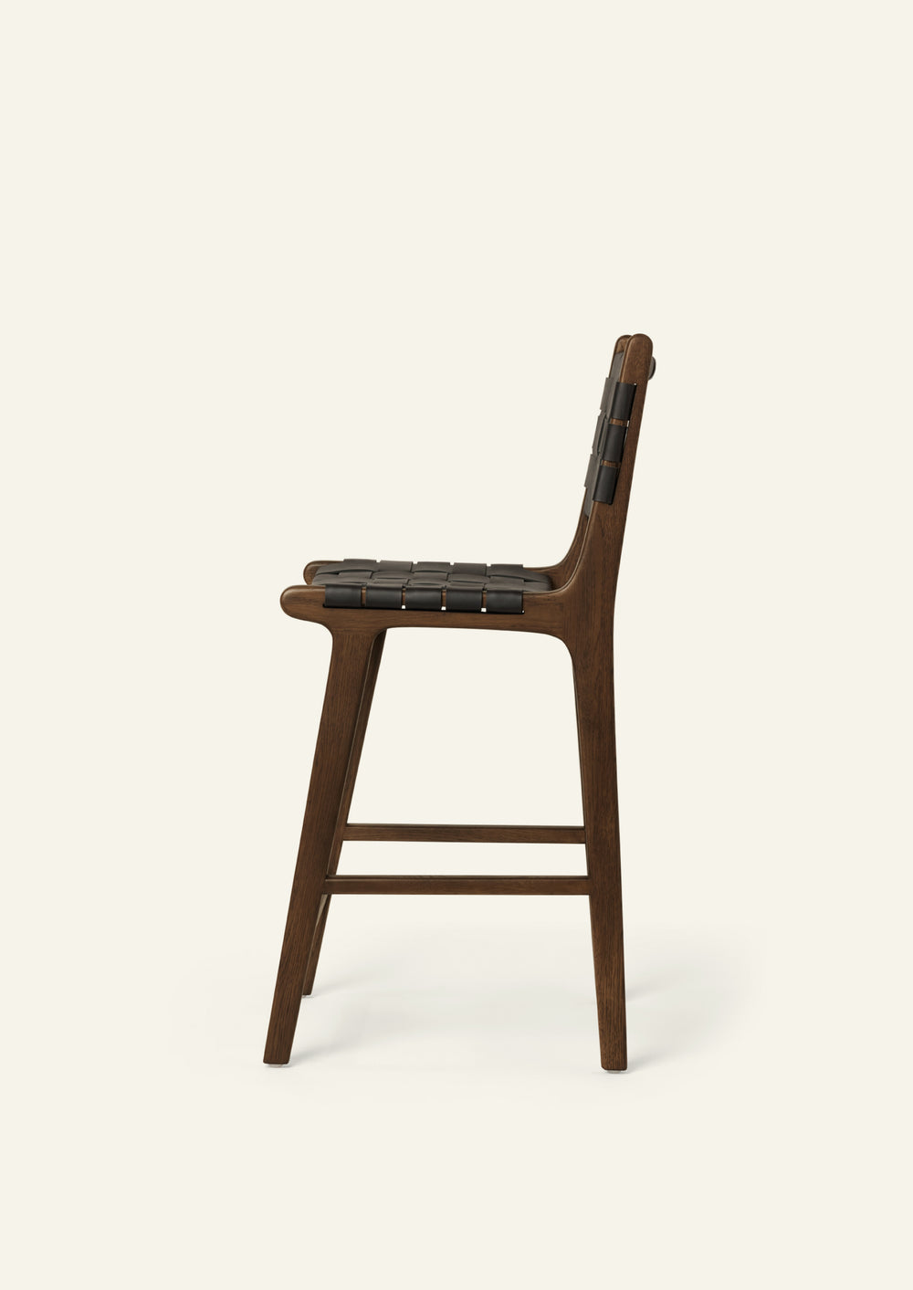 Side view of the Bali Counter Stool in solid brown oak with handwoven black leather, shown in a three-quarter view.