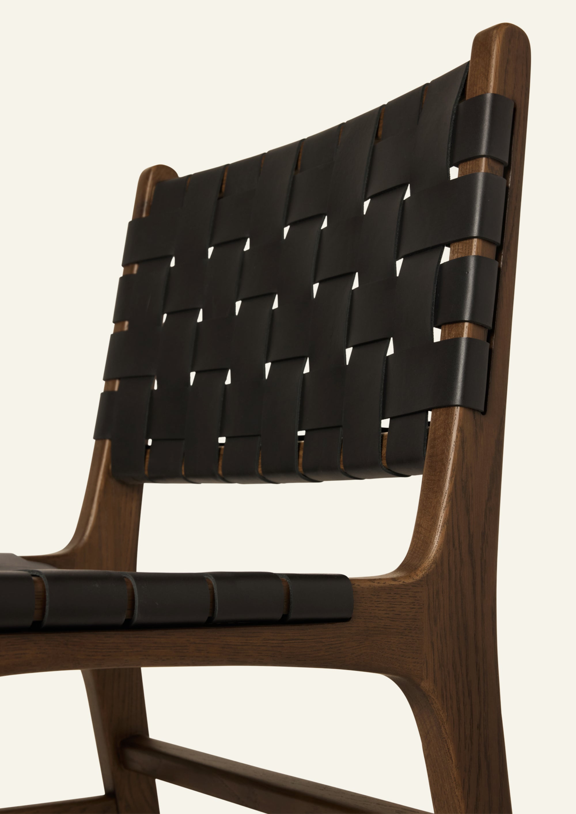 Close-up of the Bali Dining Chair highlighting the woven black leather backrest and the smooth transitions of the solid brown oak frame. The craftsmanship emphasizes both durability and texture.
