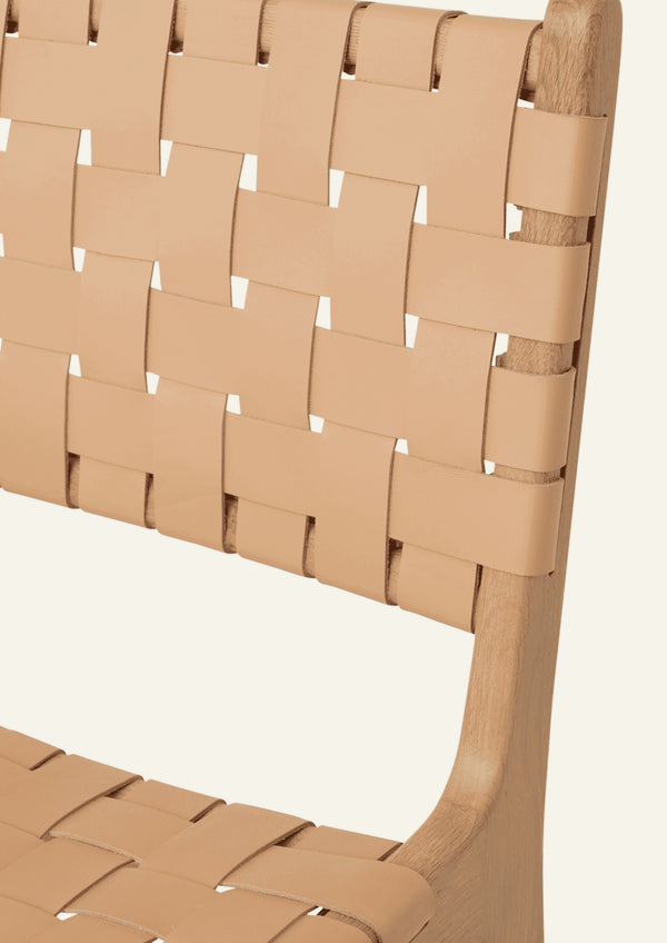 Close-up of the Bali Dining Chair highlighting the woven natural leather backrest and the smooth transitions of the solid white oak frame. The craftsmanship emphasizes both durability and texture.
