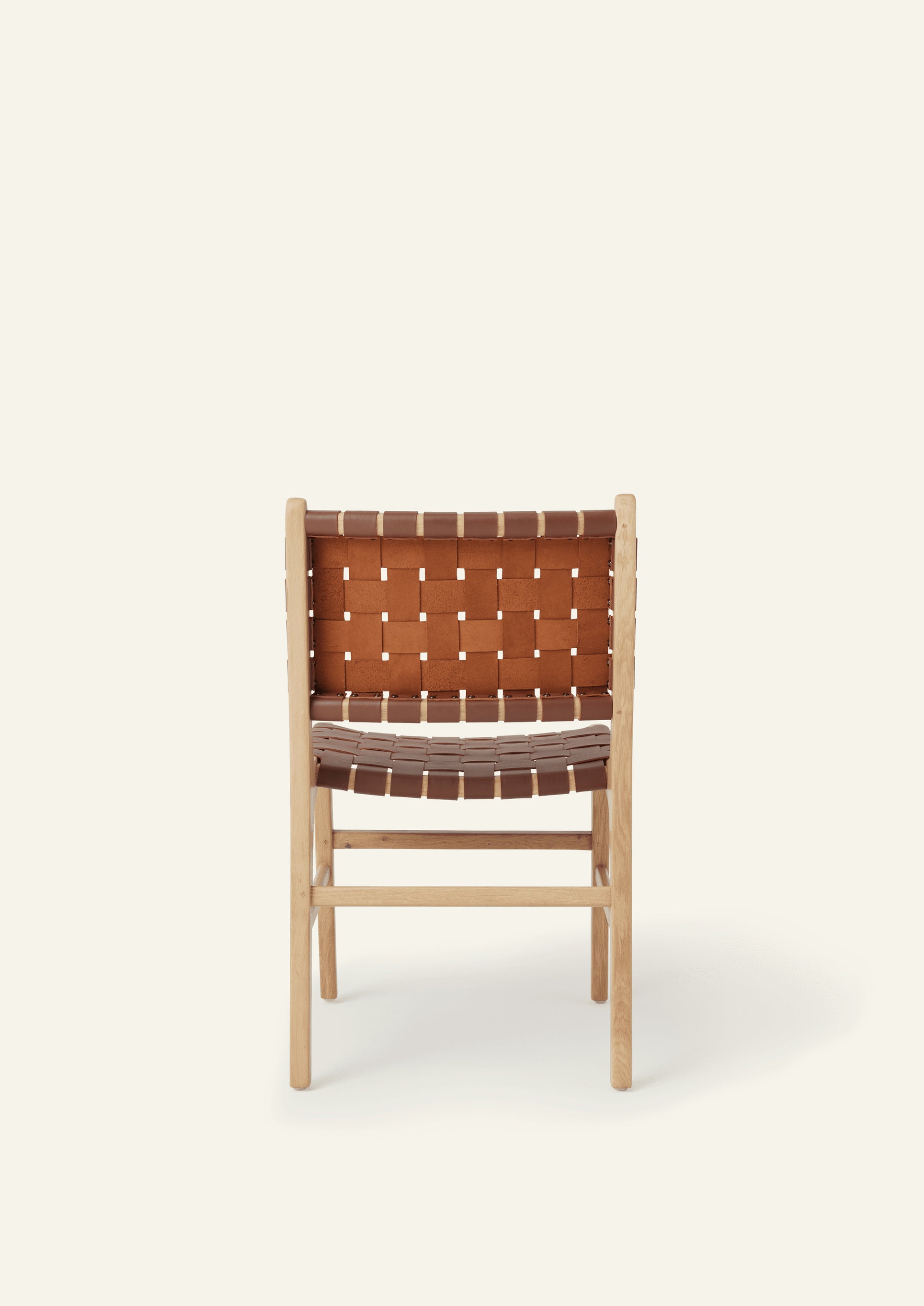 Back view of the Bali Dining Chair with a woven whiskey leather seat and back. Rounded edges, softly tapered legs, and natural materials create a warm and inviting presence.