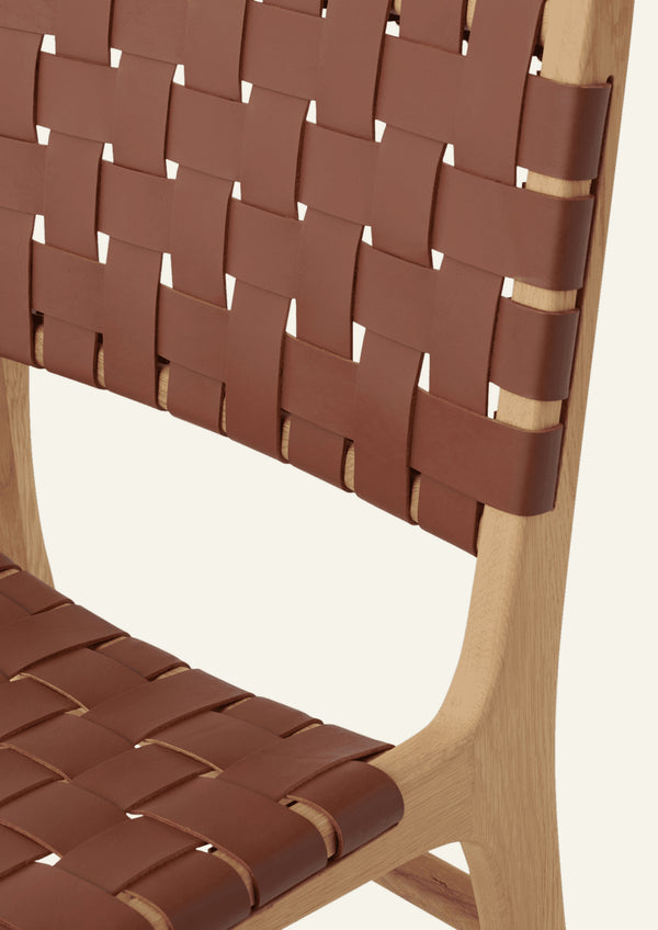 Close-up of the Bali Dining Chair highlighting the woven whiskey leather backrest and the smooth transitions of the solid white oak frame. The craftsmanship emphasizes both durability and texture.