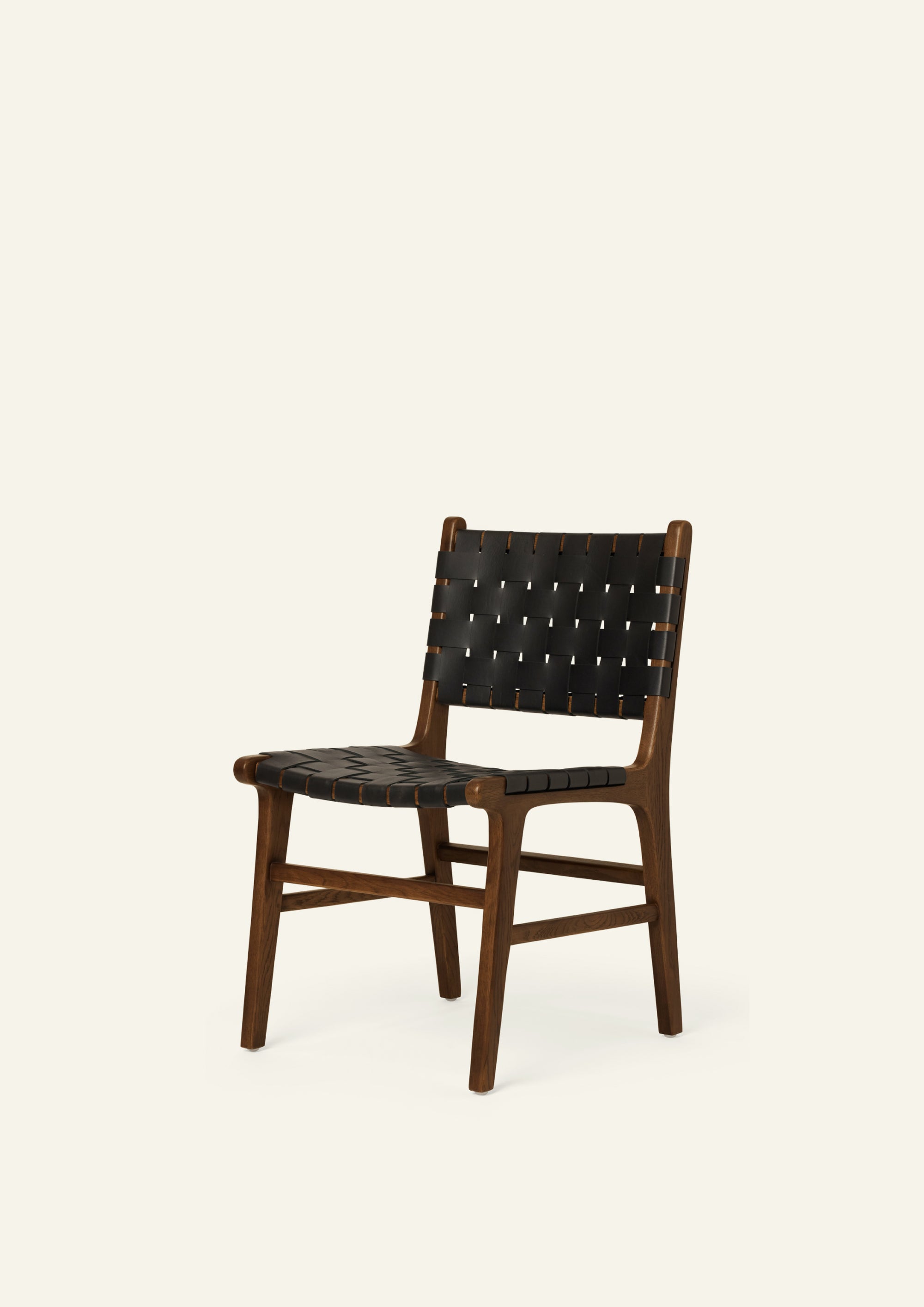 Angled view of the Bali Dining Chair with woven black full-grain leather seating and backrest. The combination of dark leather and warm oak creates a refined, contemporary look.