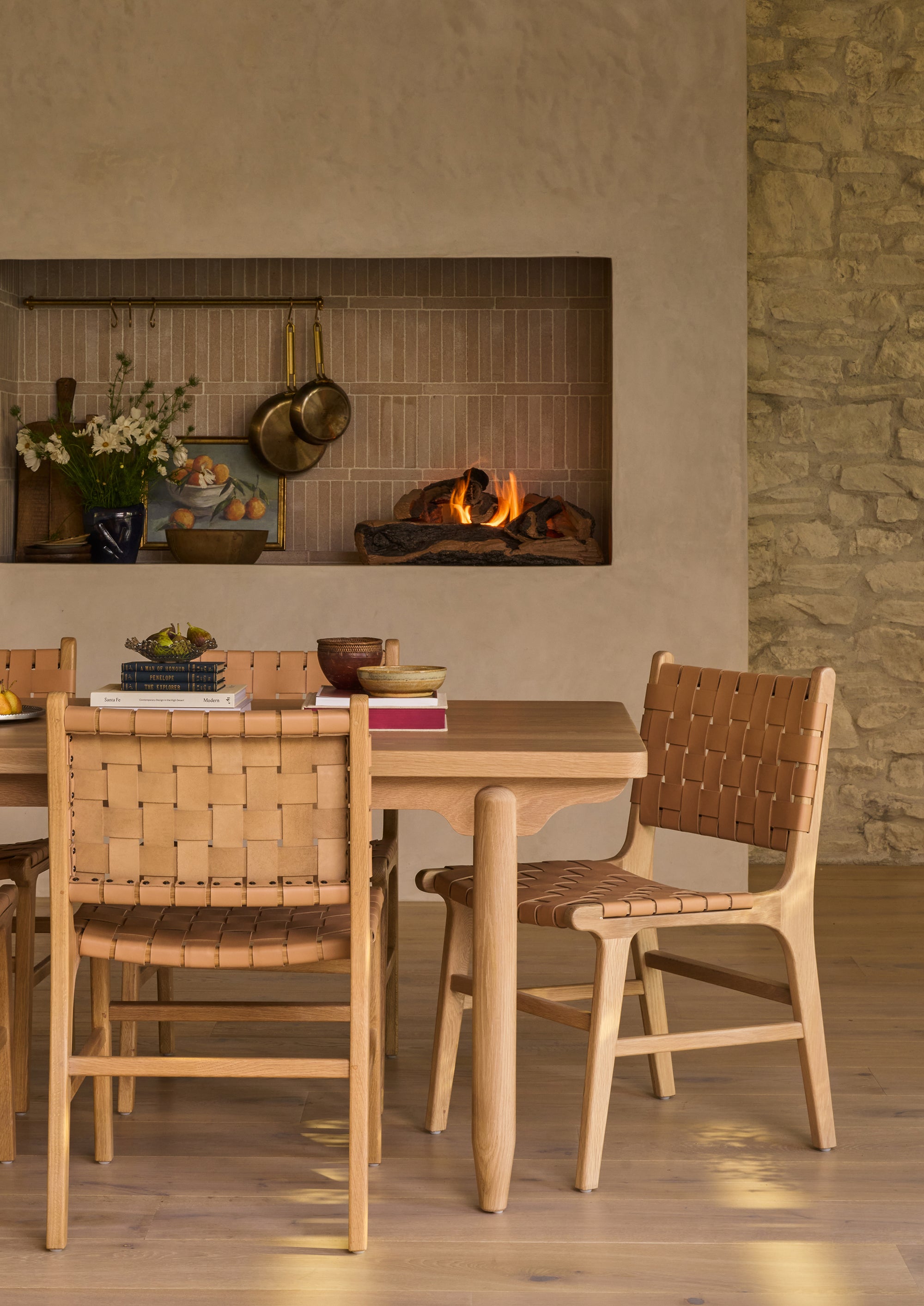 Multiple Bali Dining Chairs gathered around  the Anders white oak dining table beside a fireplace. The woven leather seats and backs add warmth, texture, and craftsmanship to the room’s organic aesthetic.