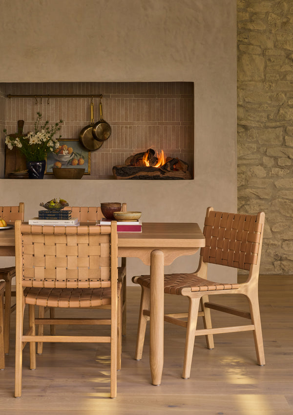 Multiple Bali Dining Chairs gathered around  the Anders white oak dining table beside a fireplace. The woven leather seats and backs add warmth, texture, and craftsmanship to the room’s organic aesthetic.