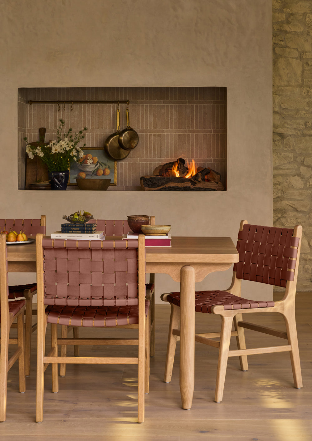 A set of Bali Dining Chairs gathered around a solid wood dining table in a welcoming dining room with a stone fireplace. The whiskey leather seating introduces warmth and character while complementing the natural white oak finishes.