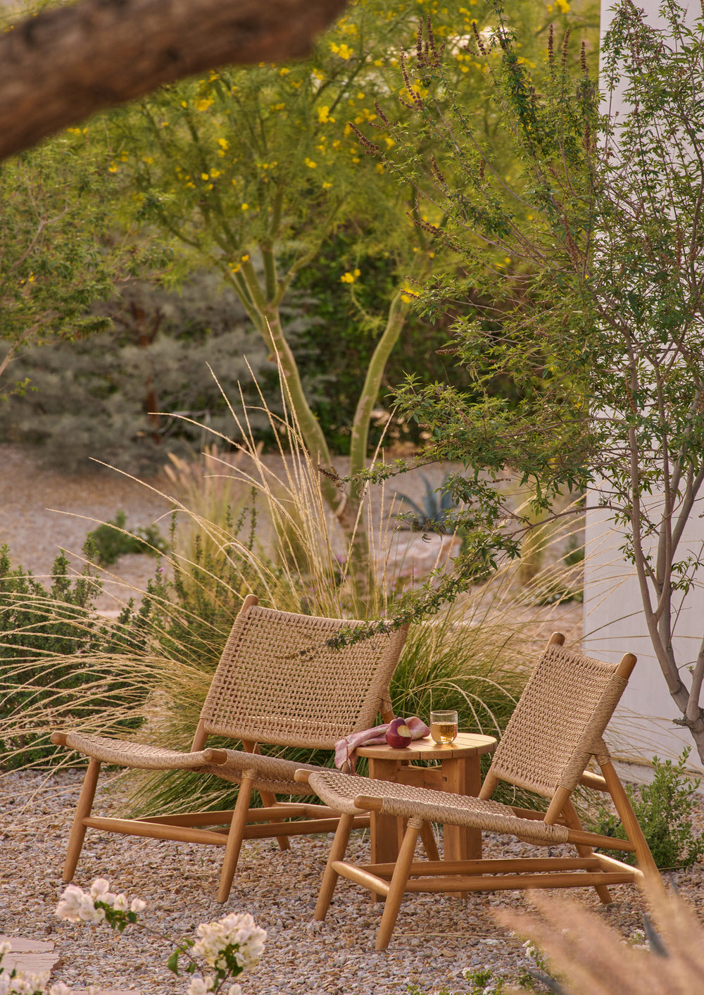 Two woven lounge chairs positioned on an outdoor terrace overlooking rolling hills. Crafted from teak and synthetic paper cord, the chairs create an inviting space for relaxation while blending naturally with the surrounding landscape.