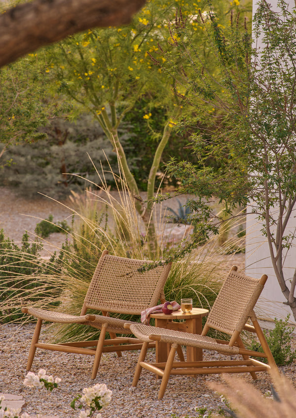 Two woven lounge chairs positioned on an outdoor terrace overlooking rolling hills. Crafted from teak and synthetic paper cord, the chairs create an inviting space for relaxation while blending naturally with the surrounding landscape.