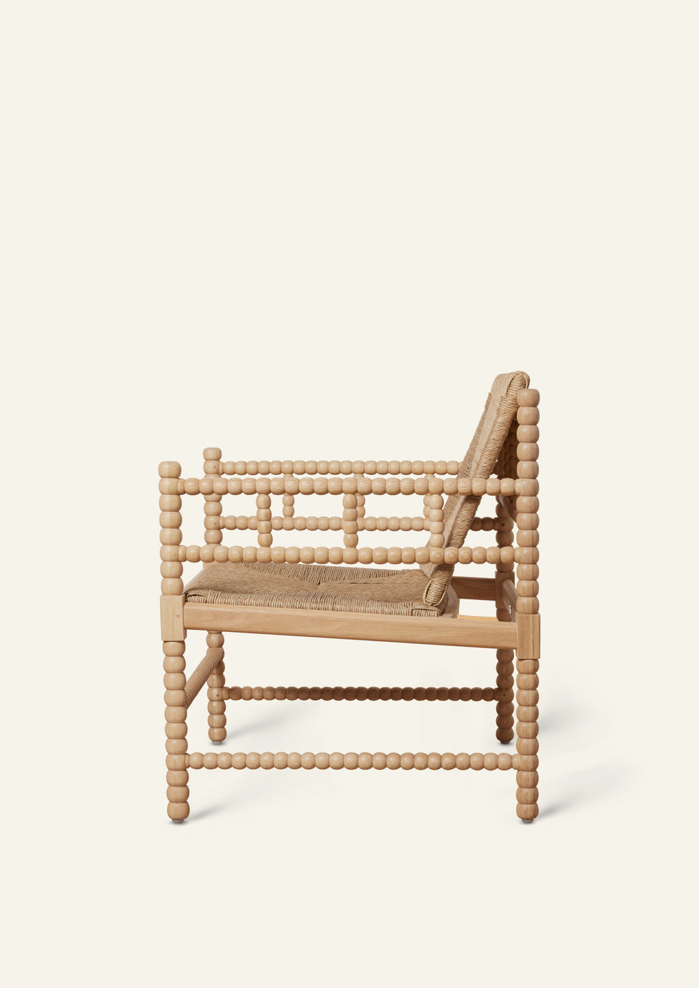 Side profile of a natural oak lounge chair featuring a handwoven rush seat and backrest. Decorative turned spindle detailing runs along the arms, legs, and stretcher supports, highlighting the chair’s handcrafted construction.
