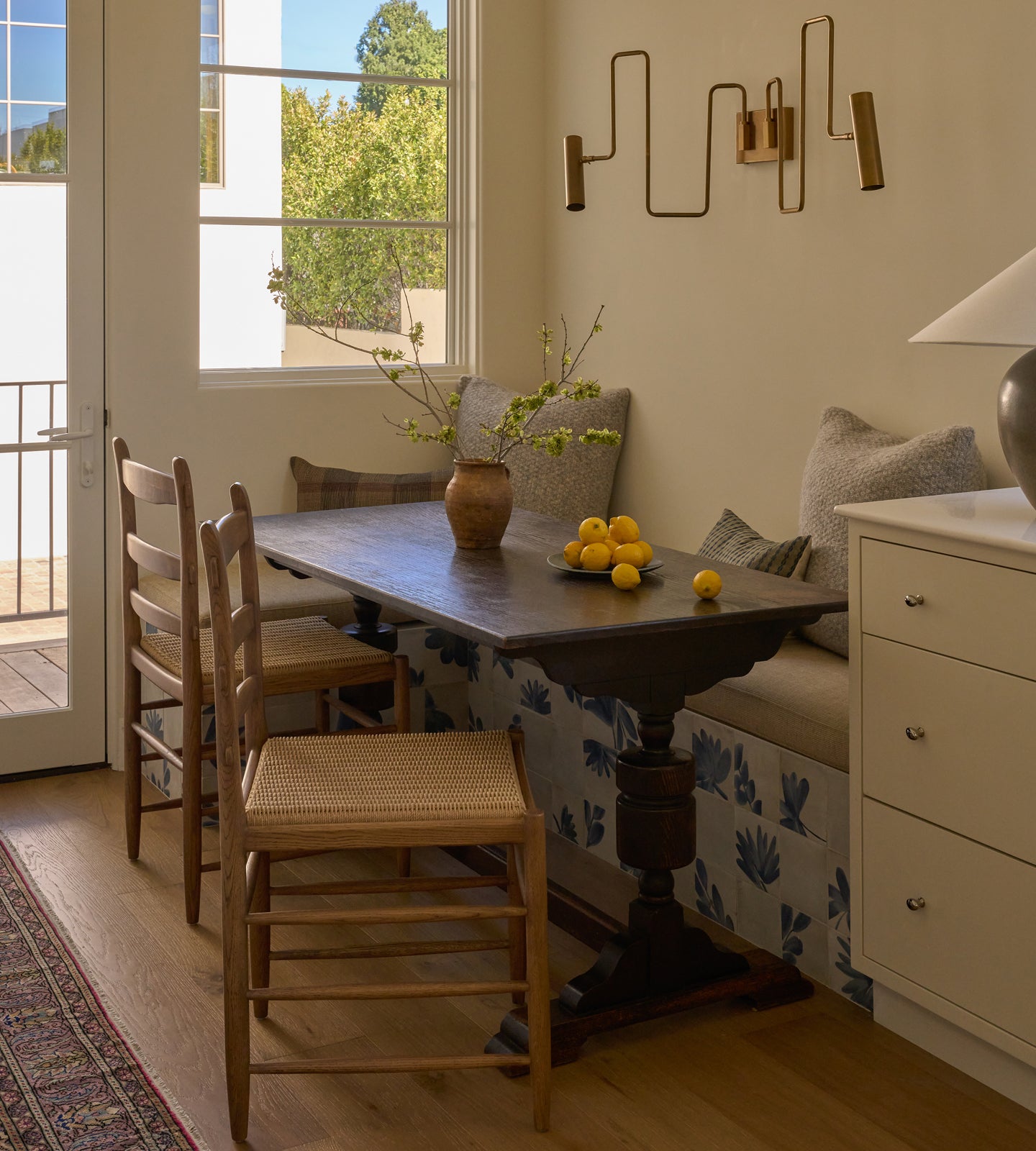 Breakfast nook area with vintage wooden table, Tiga honey oak dining chairs, and a bench with cushions in a well-lit room.