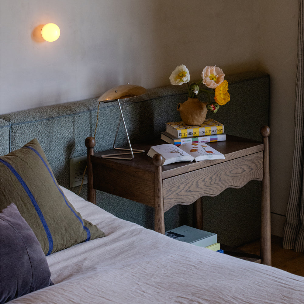 Bedroom with a bed, dark brown nightstand, and wall light fixture.
