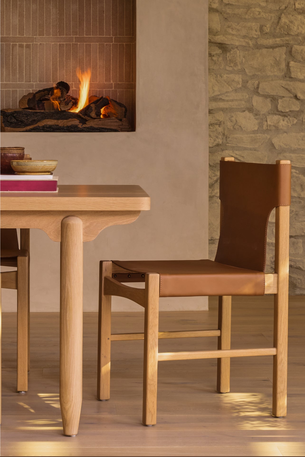Anders white oak dining table with henrik leather dining chairs in a room with a fireplace and stone wall.