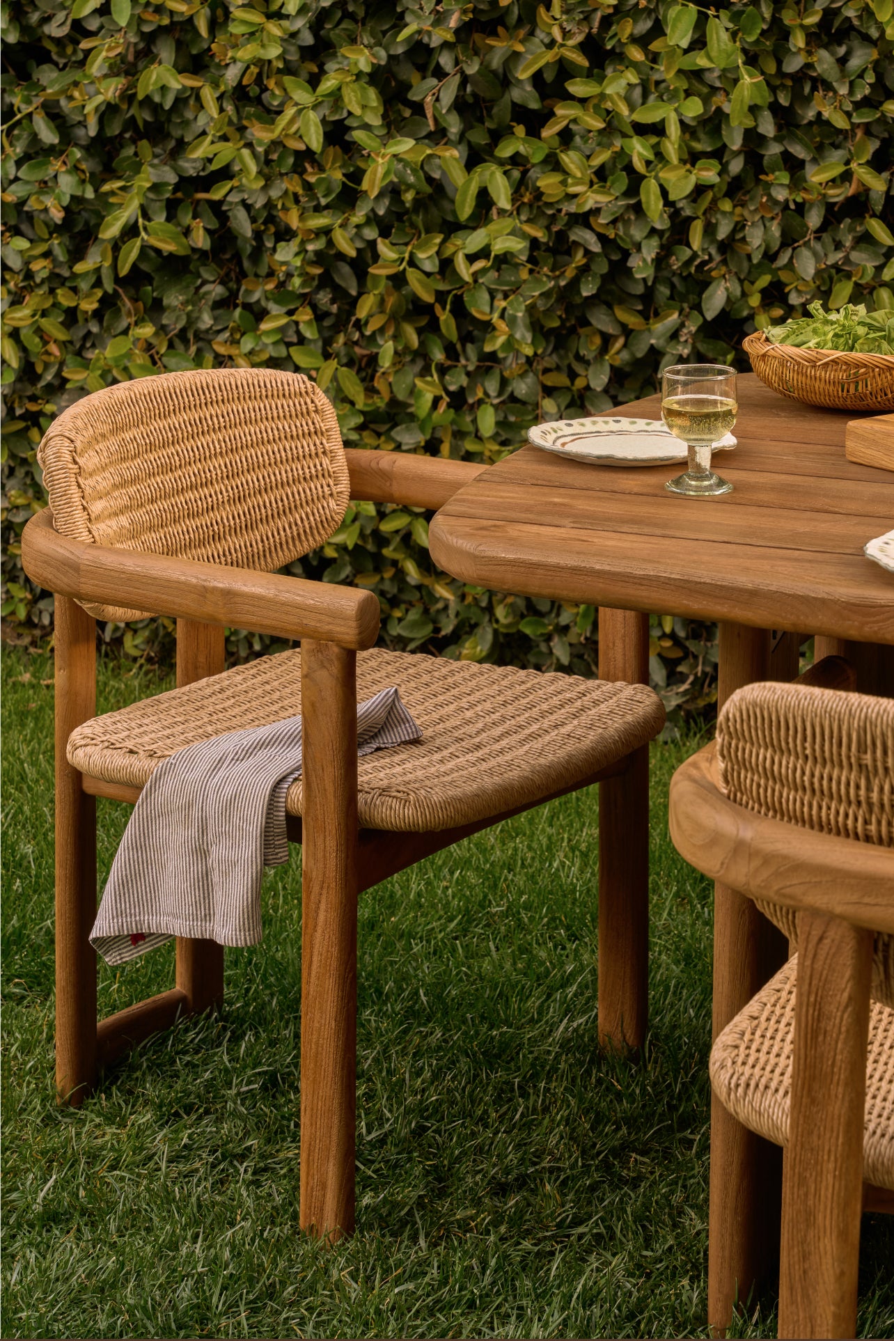 Wooden outdoor furniture set with chairs and a table against a green hedge.