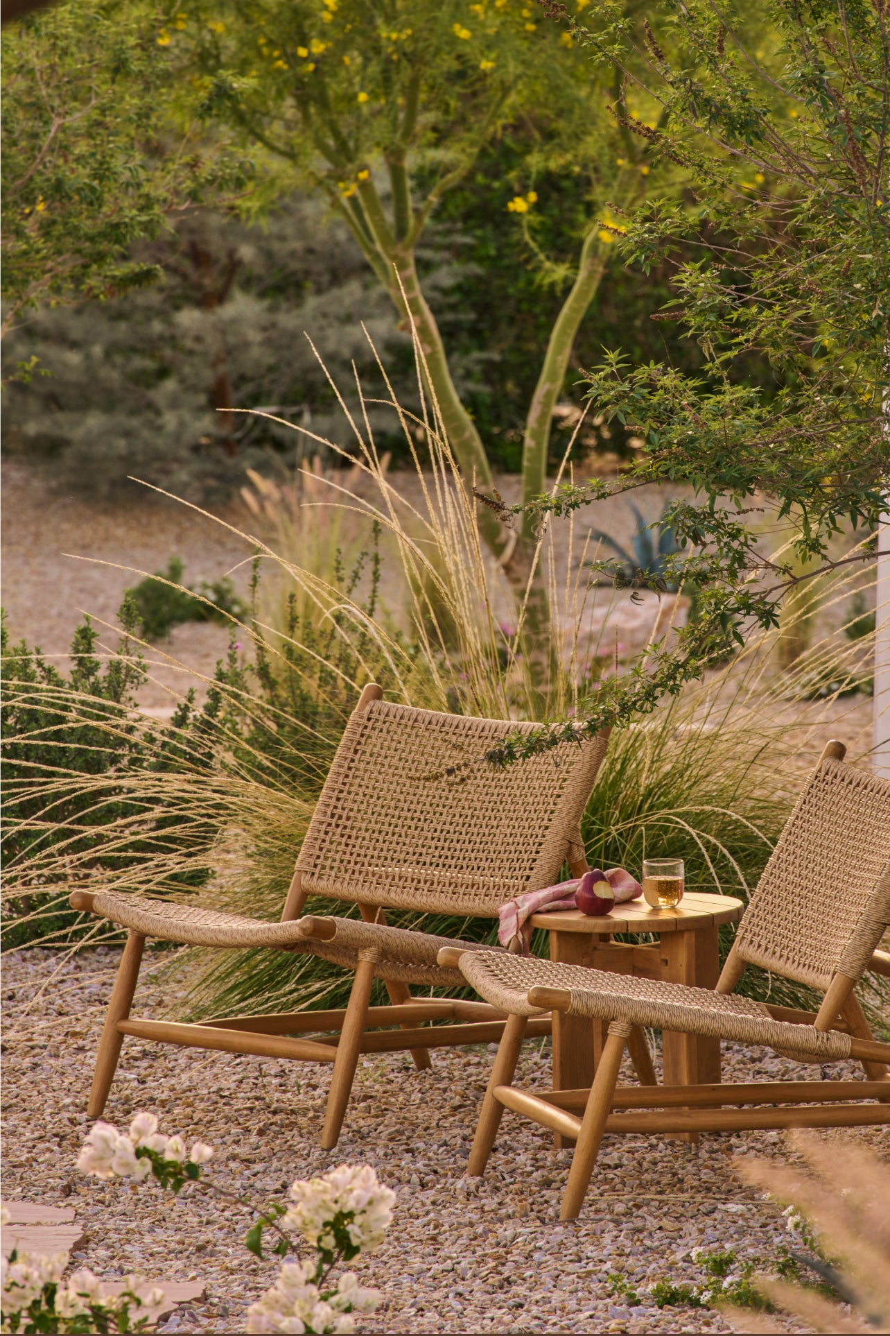 Two Bali teak lounge chairs and an Otto side table in a garden setting with plants and flowers.