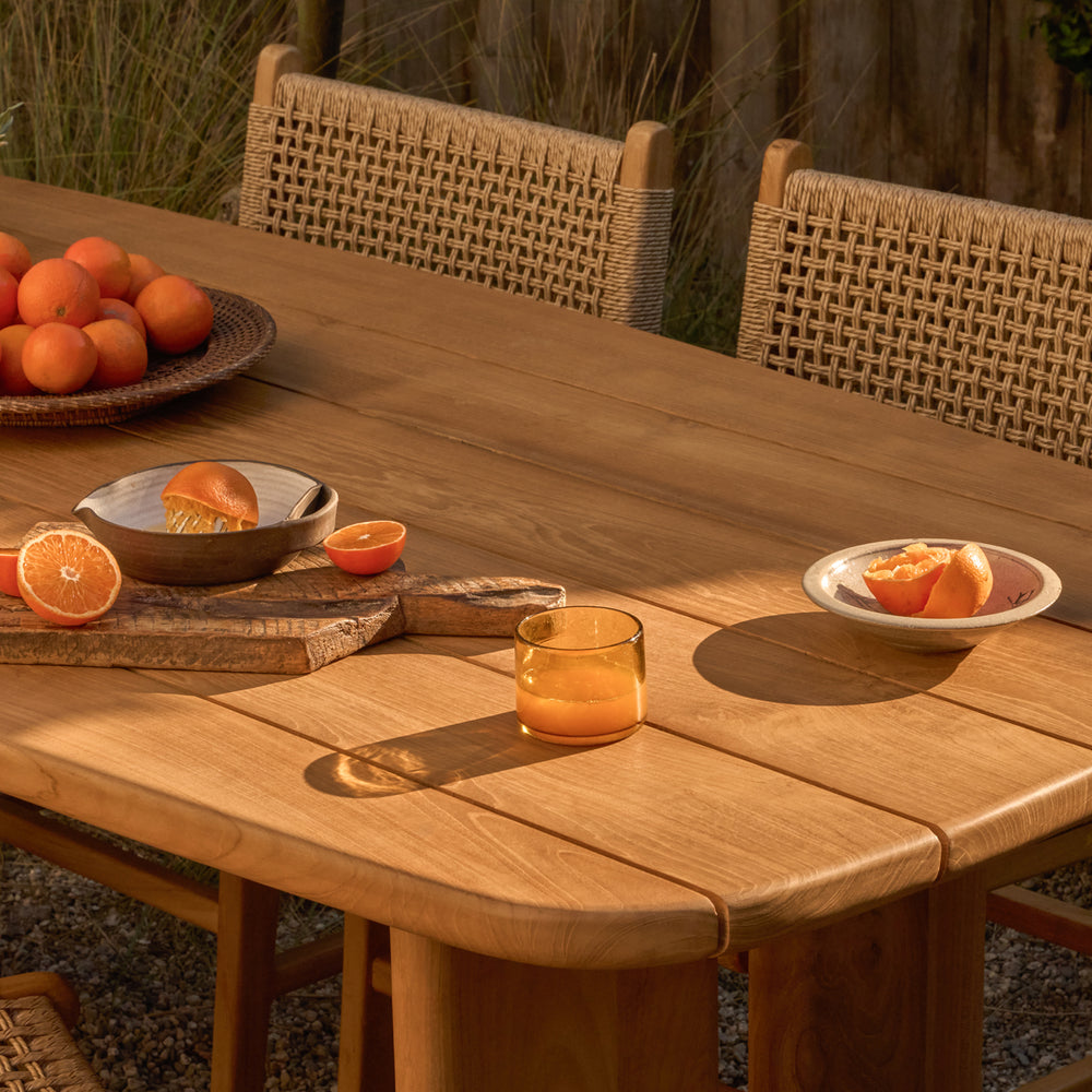 Teak outdoor table with oranges and a glass of orange juice on a patio.