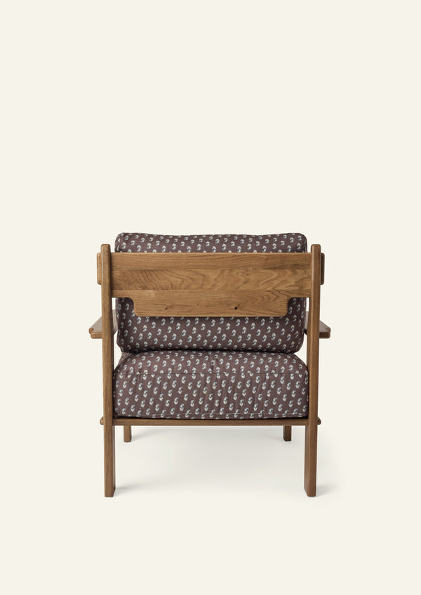 Rear view of the lounge chair showcasing the solid honey oak frame, exposed wood back panel, and Cocoa Floral upholstered cushions. Warm wood grain and thoughtful construction are visible from every angle.