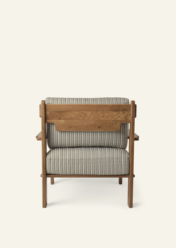 Rear view of the lounge chair showcasing the solid honey oak frame, exposed wood back panel, and Neutral Stripe upholstered cushions. Thoughtful craftsmanship highlights the chair from every angle.