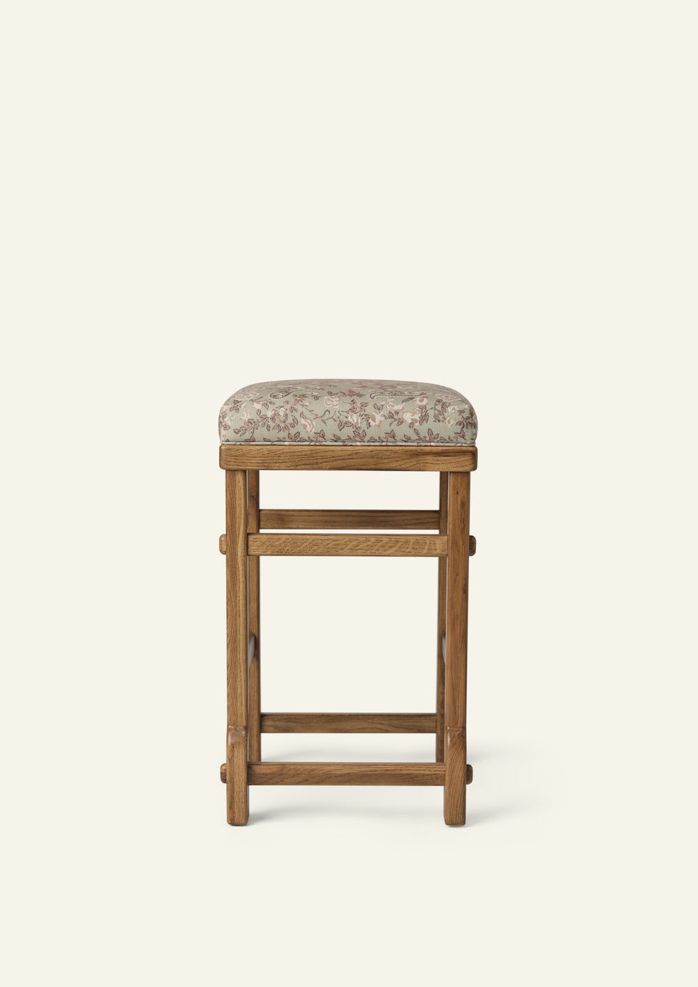 Side profile of the upholstered counter stool showing the floral cushion, solid honey oak frame, and exposed joinery details. The compact silhouette balances comfort, craftsmanship, and everyday functionality.
