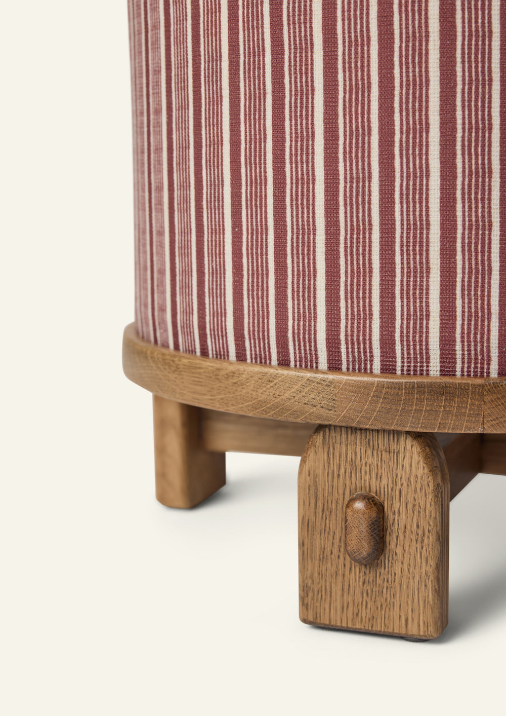 Close-up of the Yara Pouf showing the Oxblood Stripe fabric pattern and handcrafted honey oak base. The textured woven upholstery and rounded wood edge highlight the pouf’s artisanal details