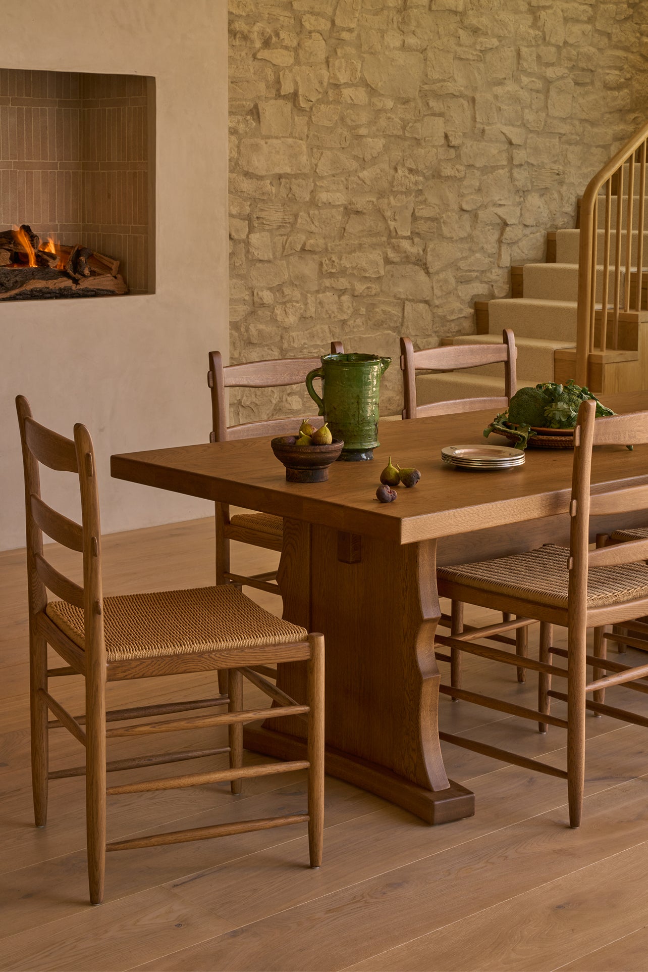Warm dining room with Etta honey oak dining table and Tiga honey oak dining chairs against a stone wall.