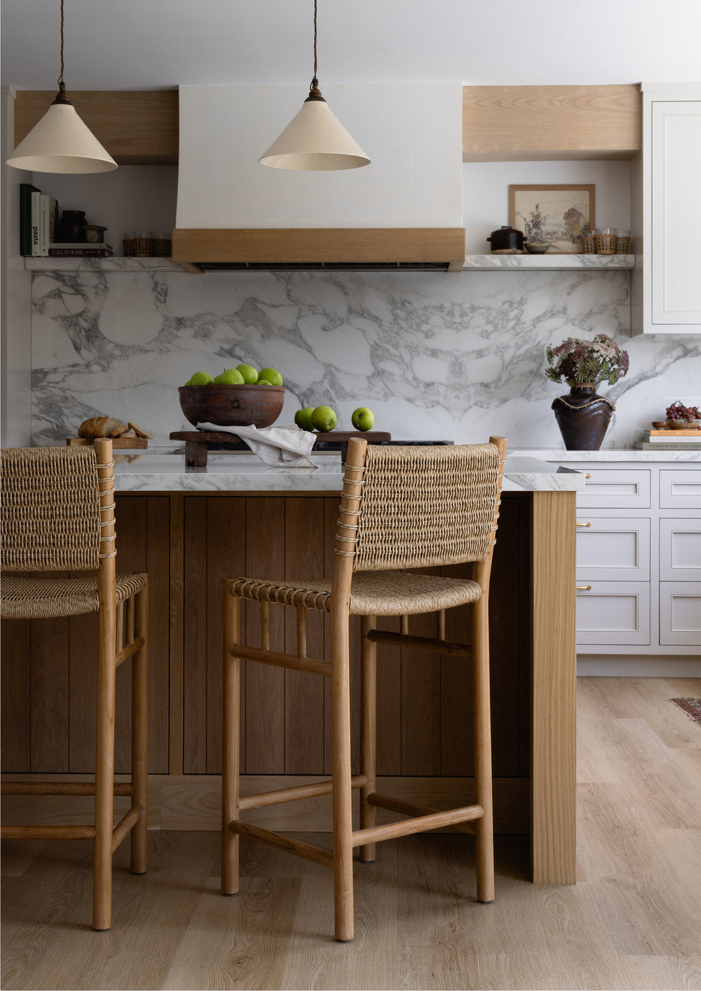 Woven counter stools arranged around a kitchen island with marble countertops and warm wood cabinetry. The natural textures and timeless silhouette create an inviting gathering space for everyday living.