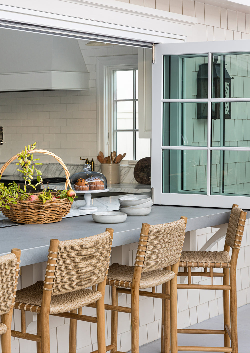 Row of counter stools at an exterior kitchen countertop with charming shingles around the window frame. 