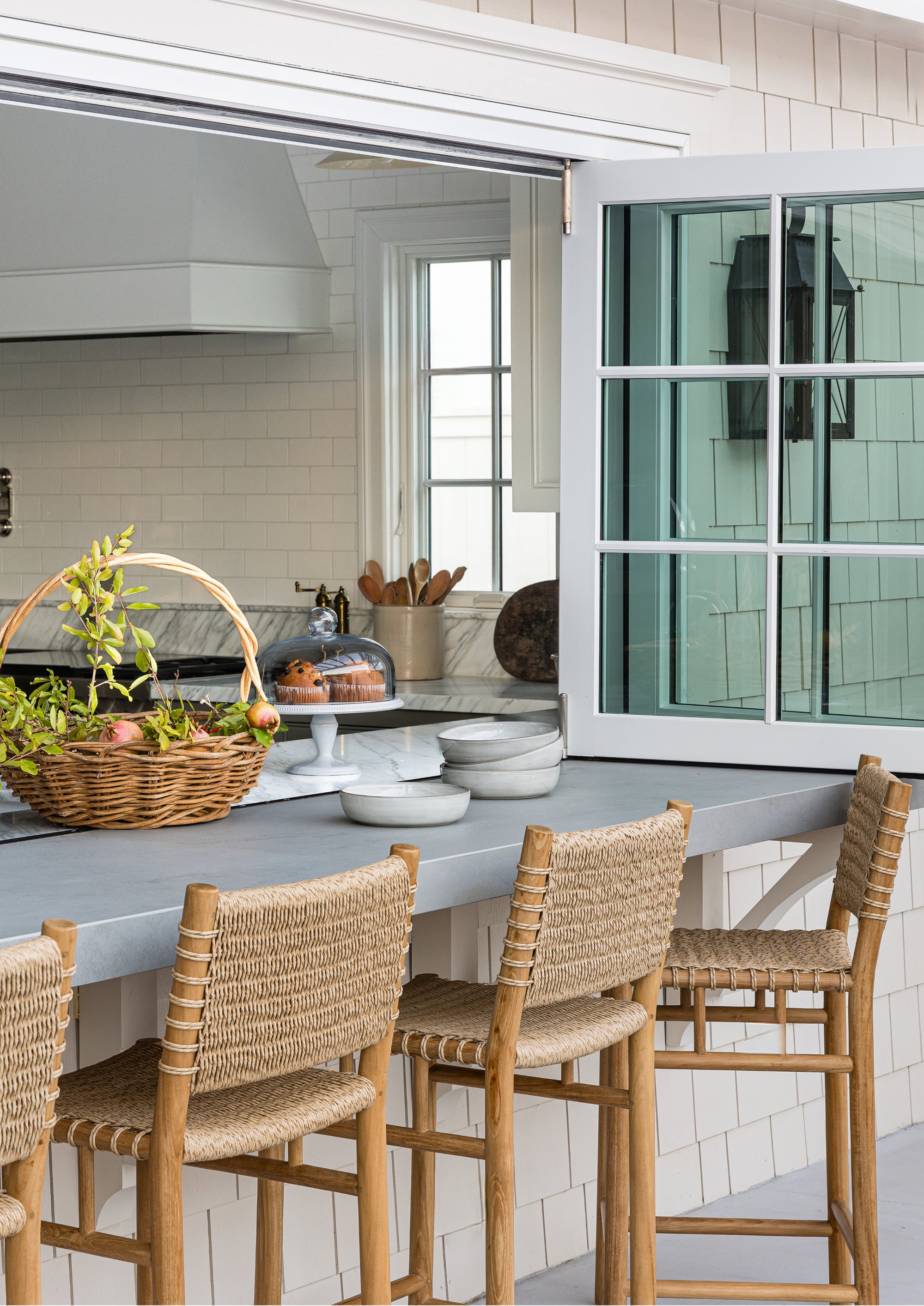 Row of counter stools at an exterior kitchen countertop with charming shingles around the window frame. 