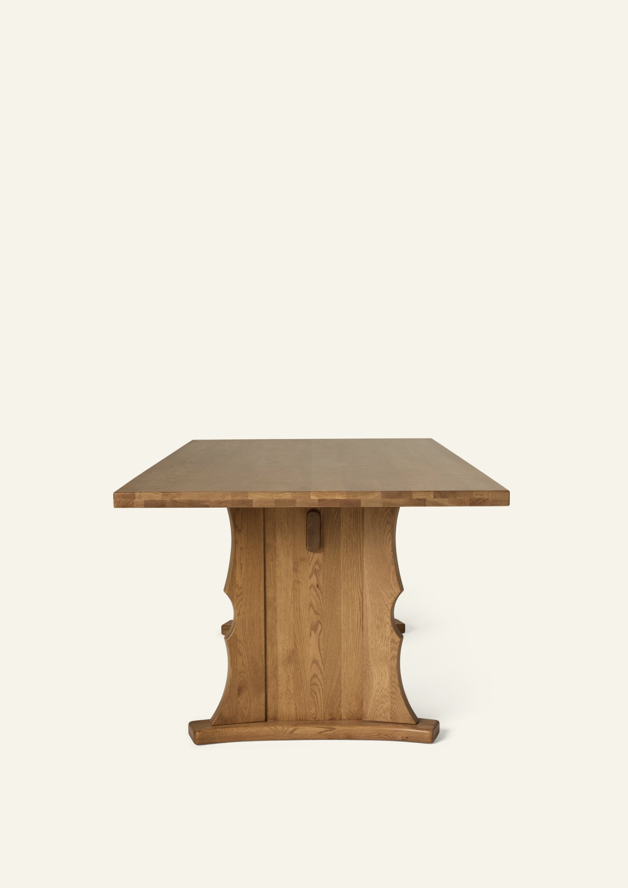 Front view of the trestle dining table showcasing its solid oak construction, thick tabletop, and sculptural pedestal base. The balanced proportions and center stretcher provide both visual weight and functional stability.
