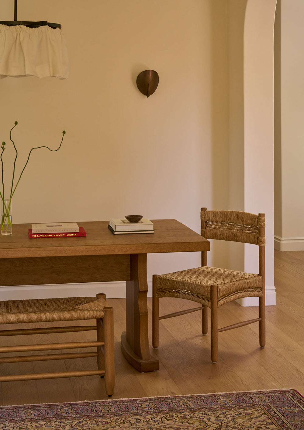 Etta honey oak dining table with a Suma dining chair  and the Mina natural rush bench in a room with a neutral color palette. 