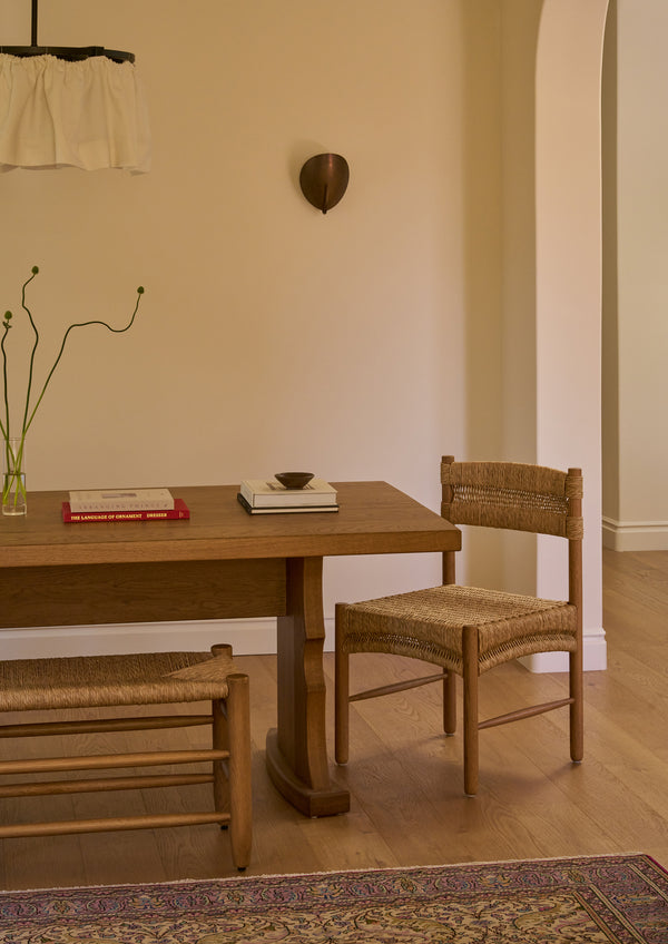 Etta honey oak dining table with a Suma dining chair  and the Mina natural rush bench in a room with a neutral color palette. 