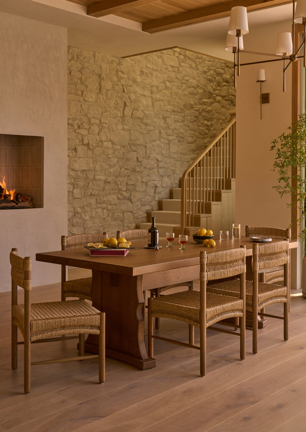 Etta honey oak dining table with the Suma natural rush dining chair in a European styled dining room with a fireplace and rock wall. 