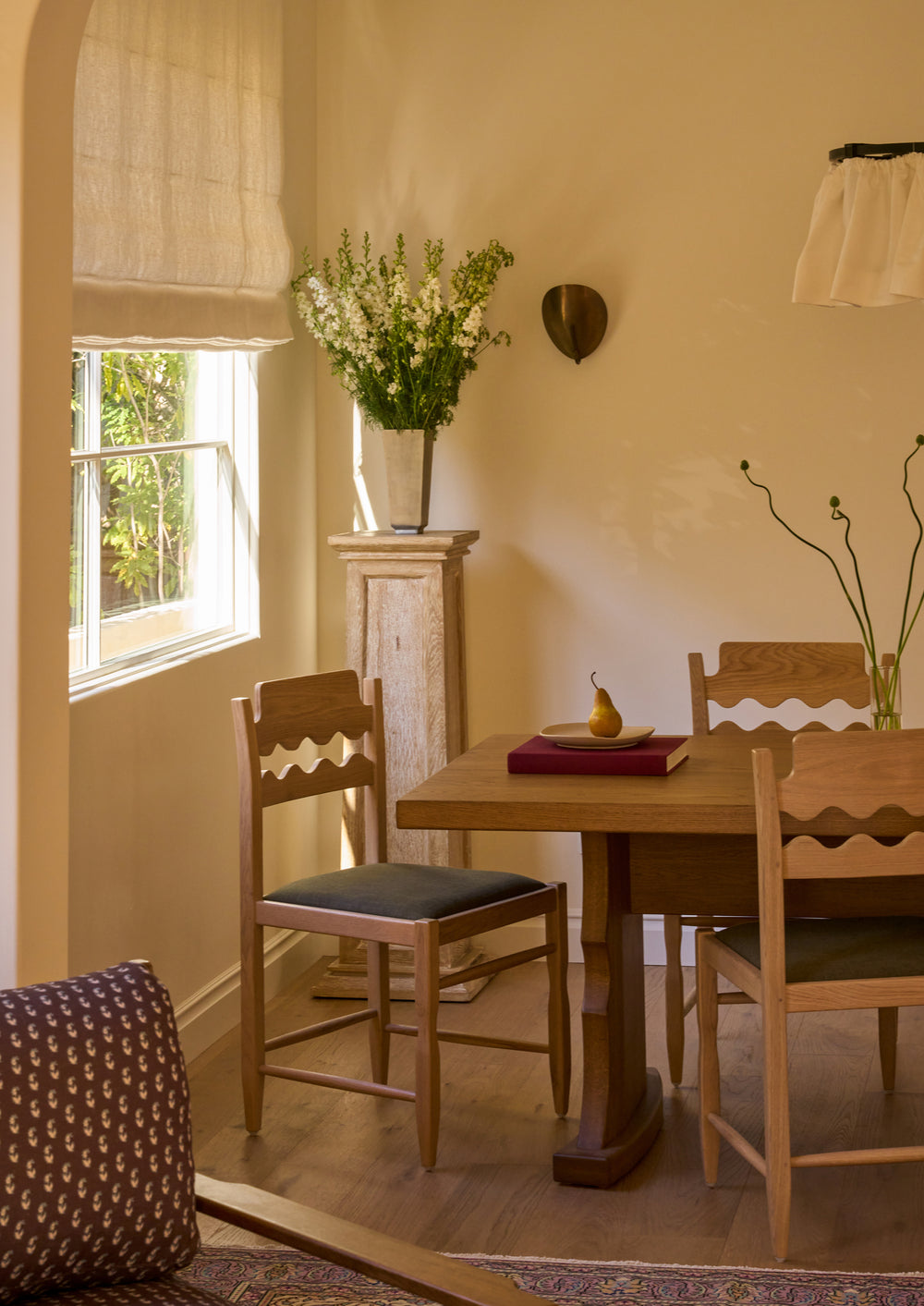 Etta honey oak dining table with a Freda Razor dining chair in an upholstered green seat in a room with a neutral color palette. 