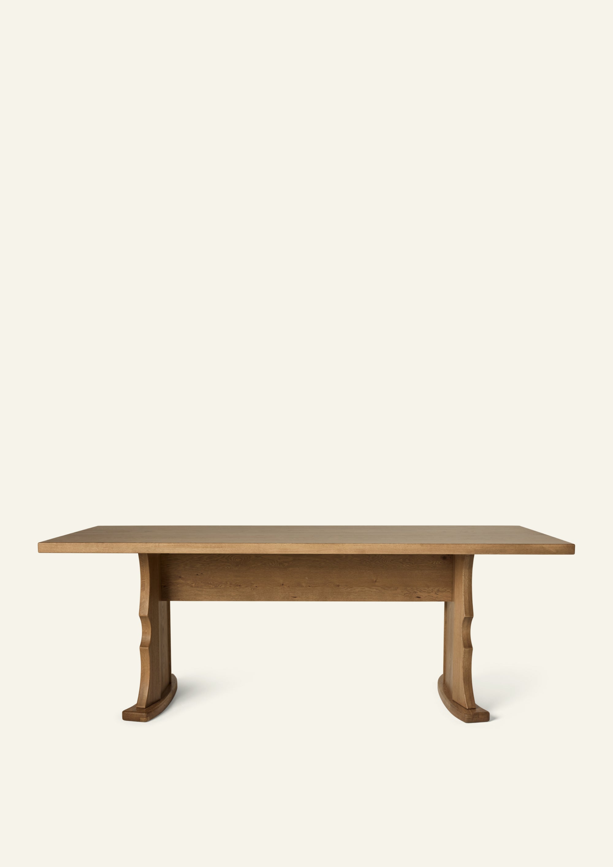 Side profile of the trestle dining table highlighting the sculptural pedestal base, center stretcher, and substantial tabletop. The architectural design balances strength and elegance while maximizing seating flexibility.