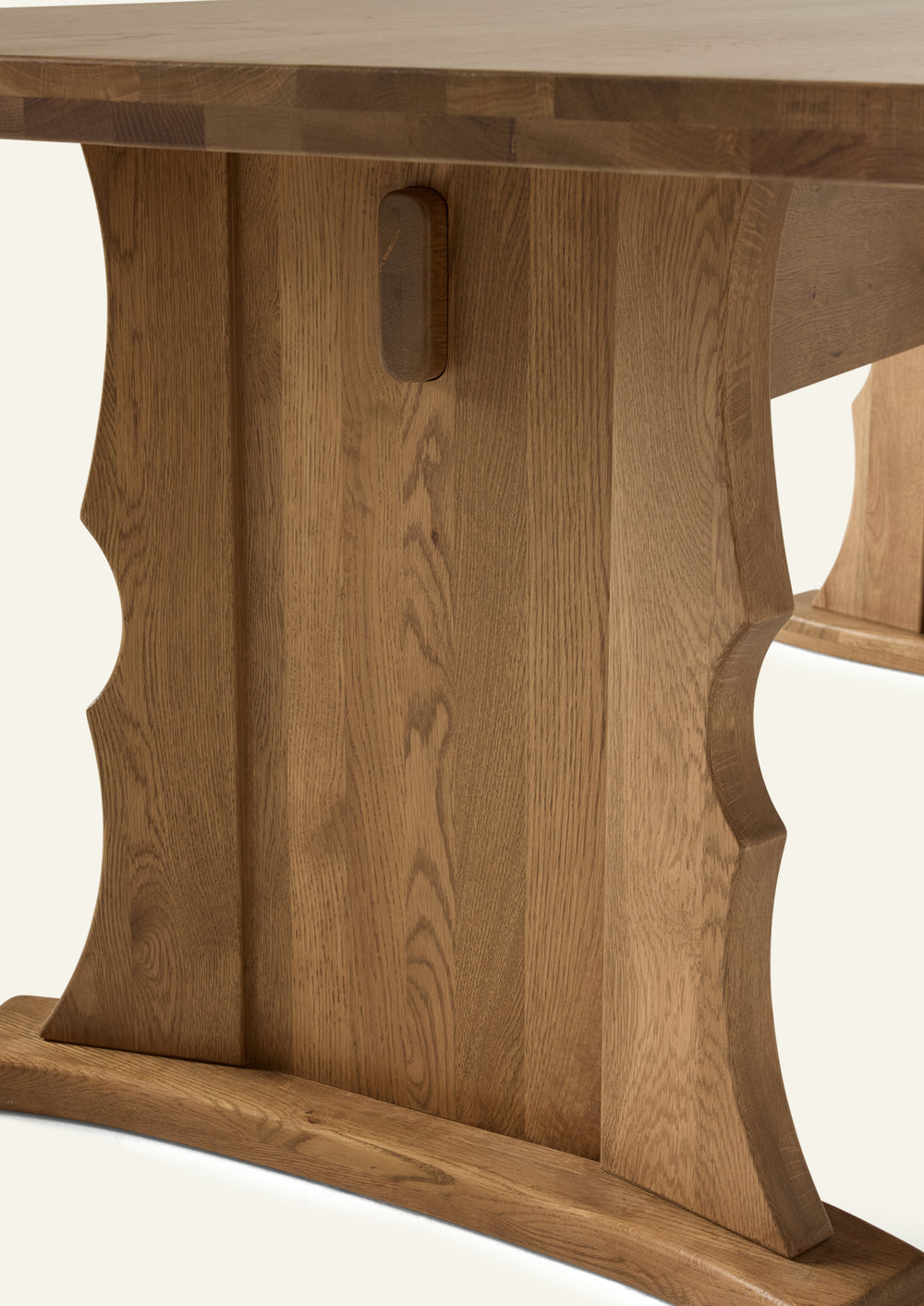 Close-up of the table’s trestle base, highlighting the sculpted silhouette, exposed joinery detail, and rich oak grain. Thoughtfully shaped curves add softness to the table’s bold, grounded form.