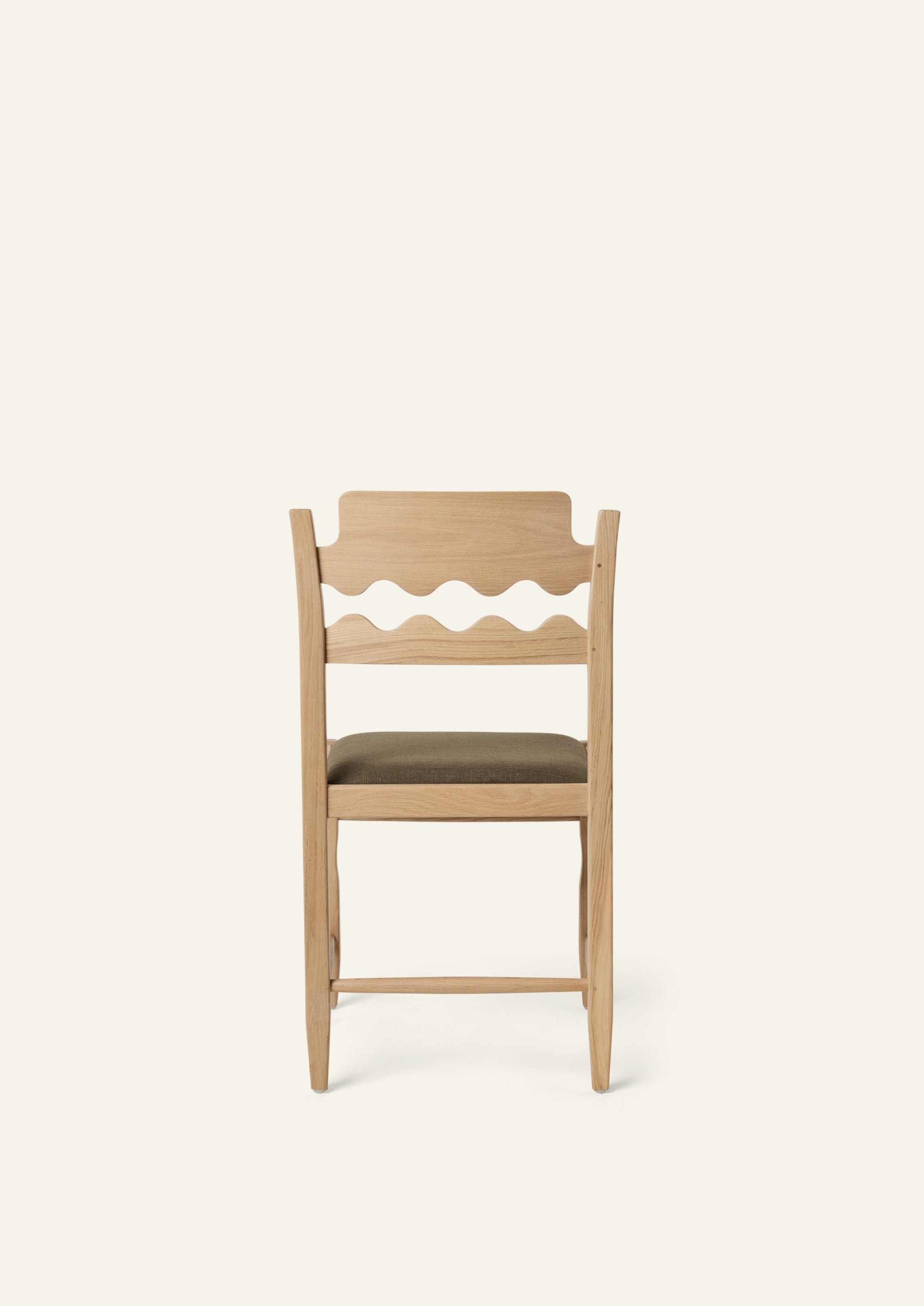 Back view of the Freda Razor Dining Chair in natural oak with an upholstered performance olive linen seat. The hand-carved scalloped backrest adds a playful yet timeless detail.